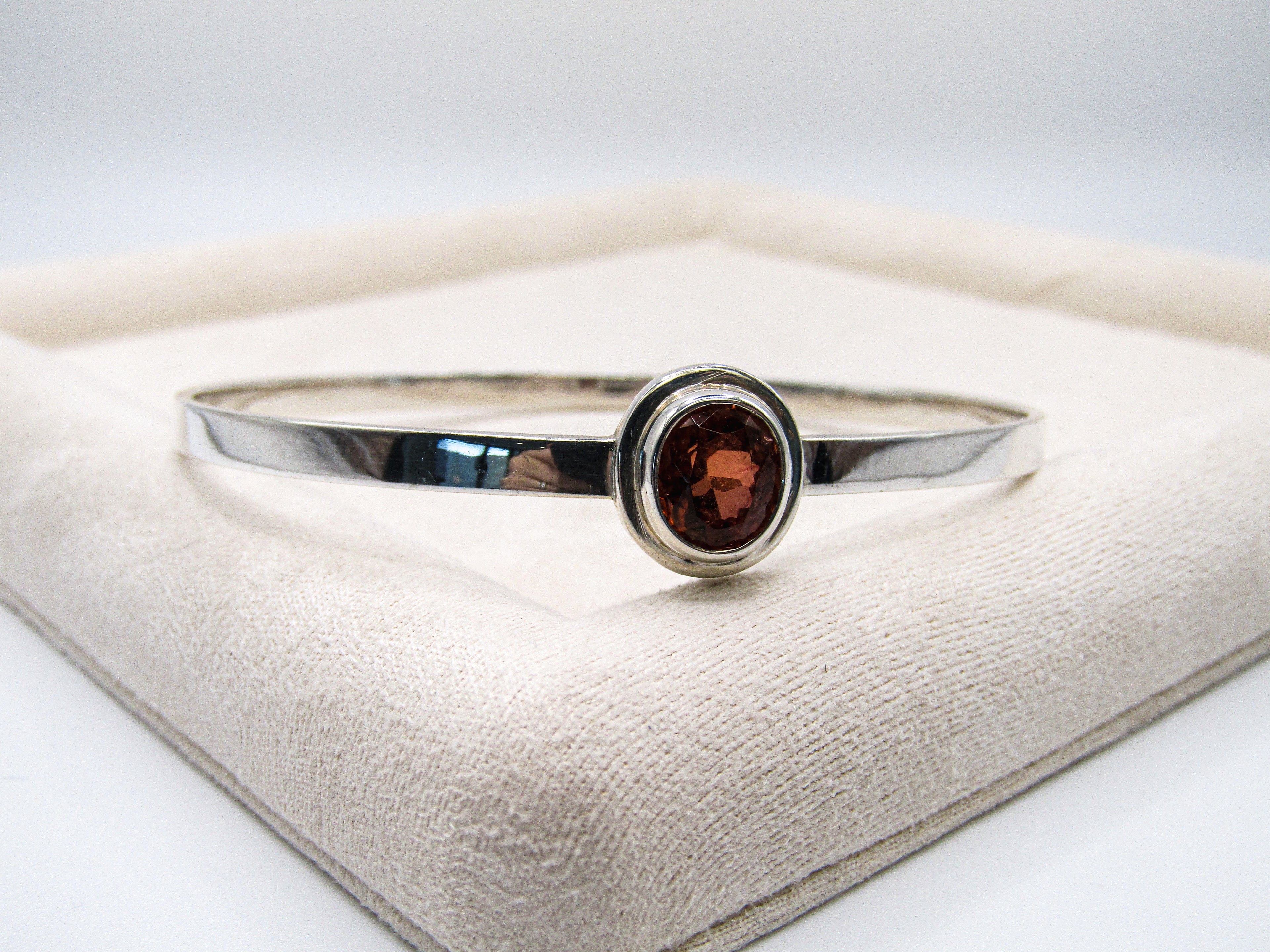 Silver ring with a red gemstone on a white cushion
