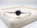 Silver bracelet with a purple gemstone on a white surface