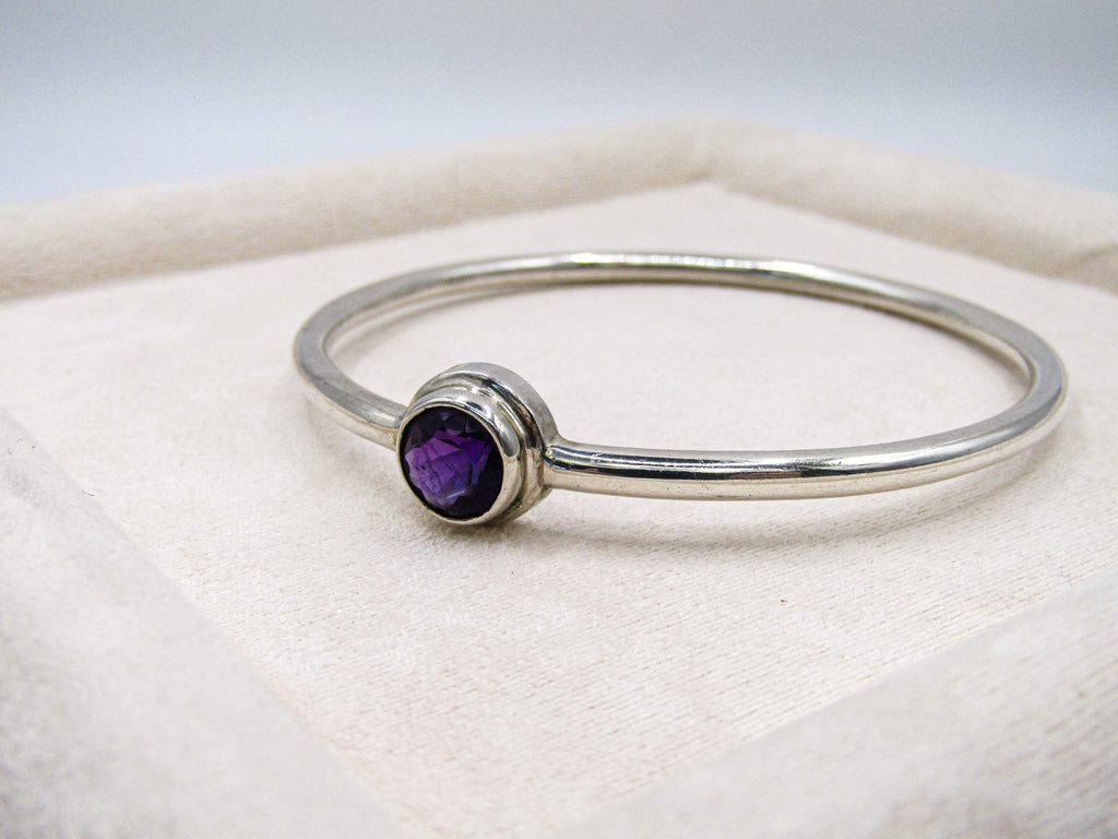 Silver bracelet with a purple gemstone on a white fabric background