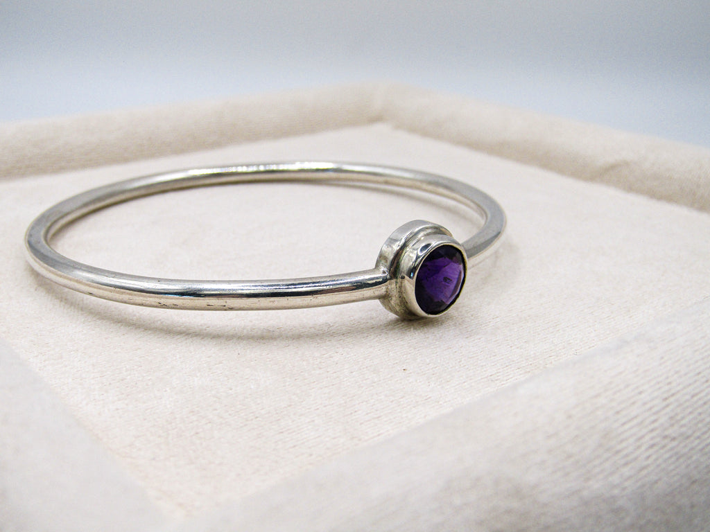 Silver bracelet with a purple gemstone on a white cushion