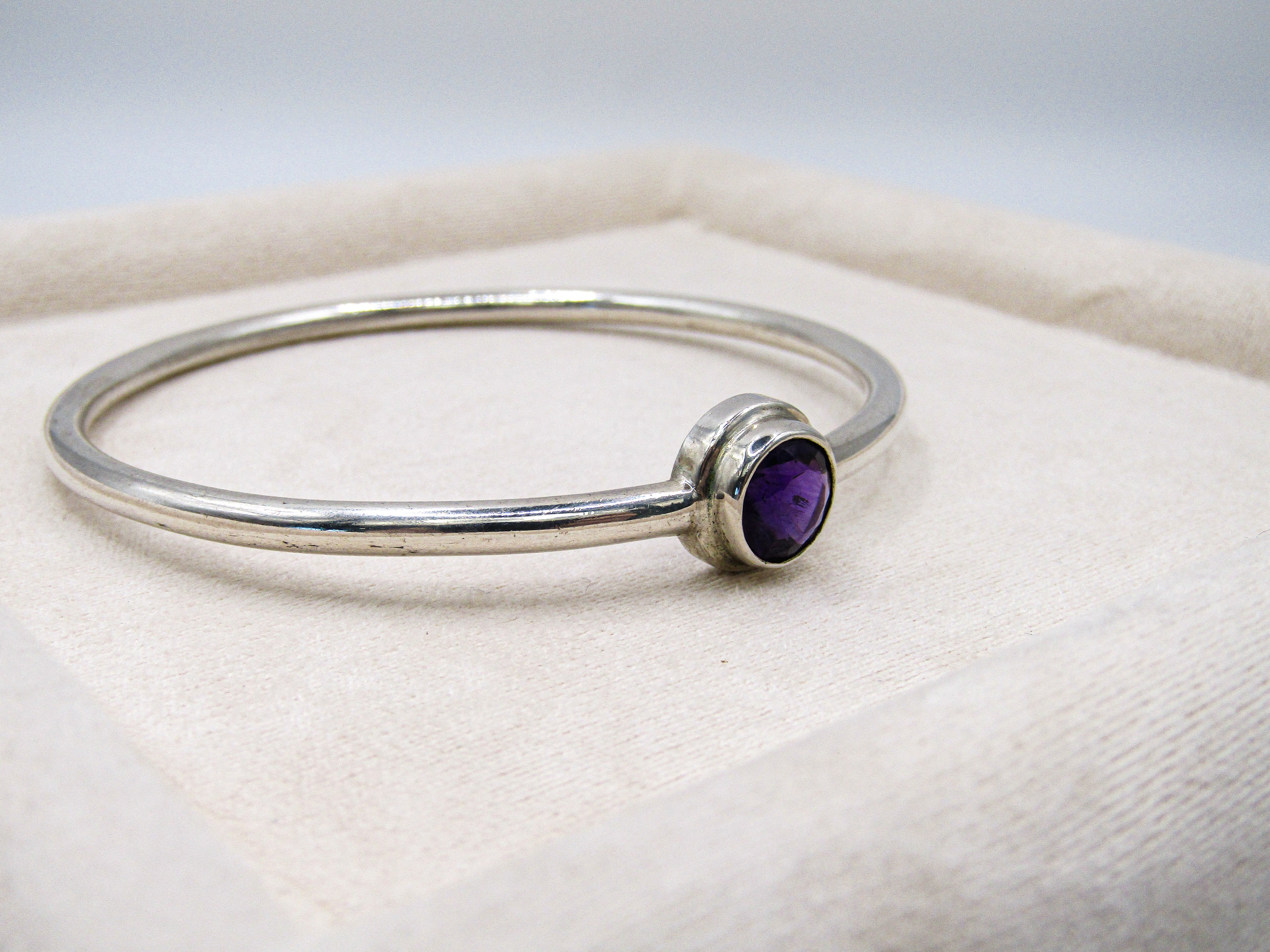 Silver bracelet with a purple gemstone on a white cushion