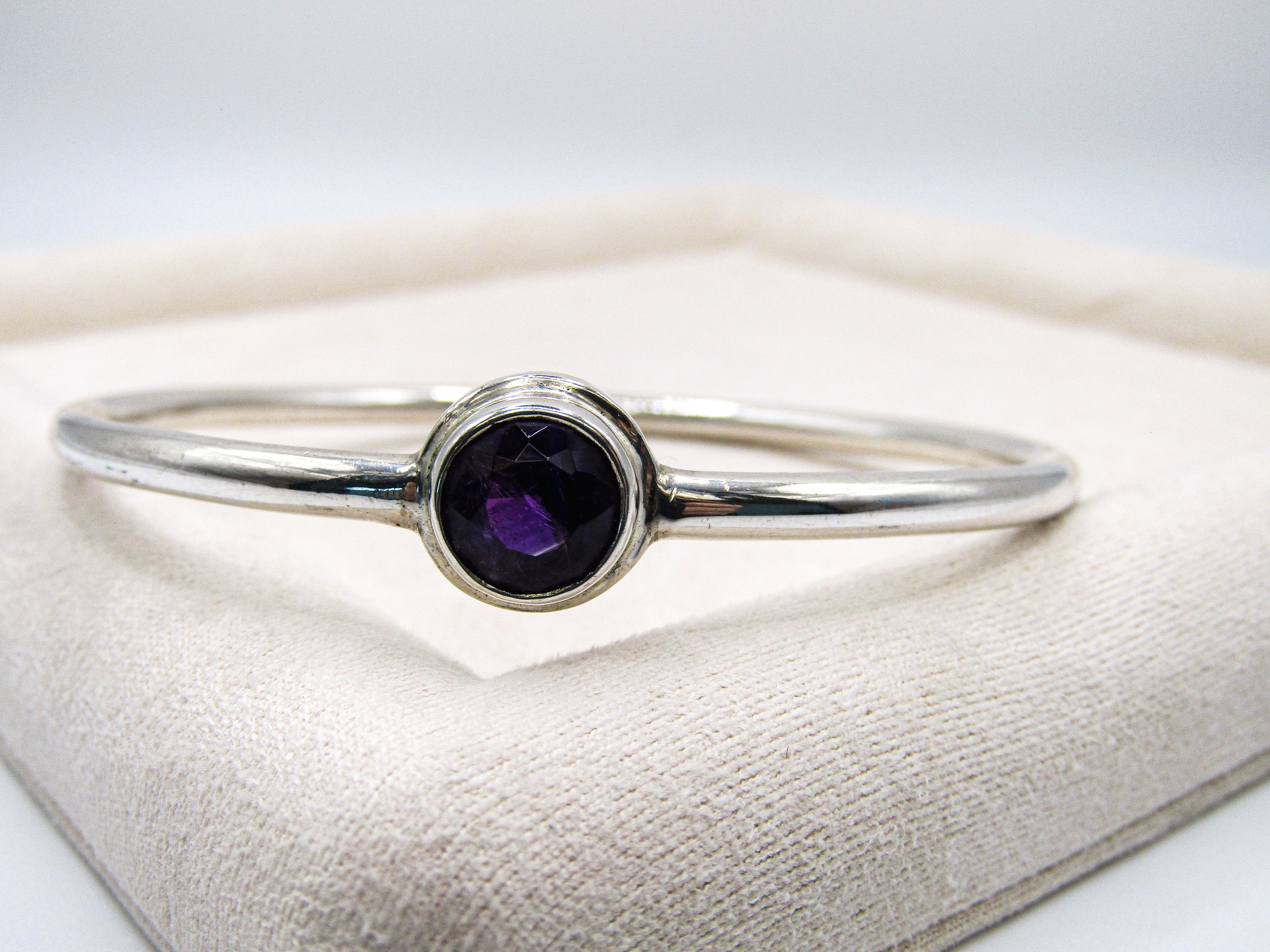 Silver bracelet with a purple gemstone on a white cushion