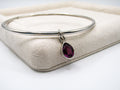 Silver bangle with a teardrop-shaped purple gemstone on a beige fabric background