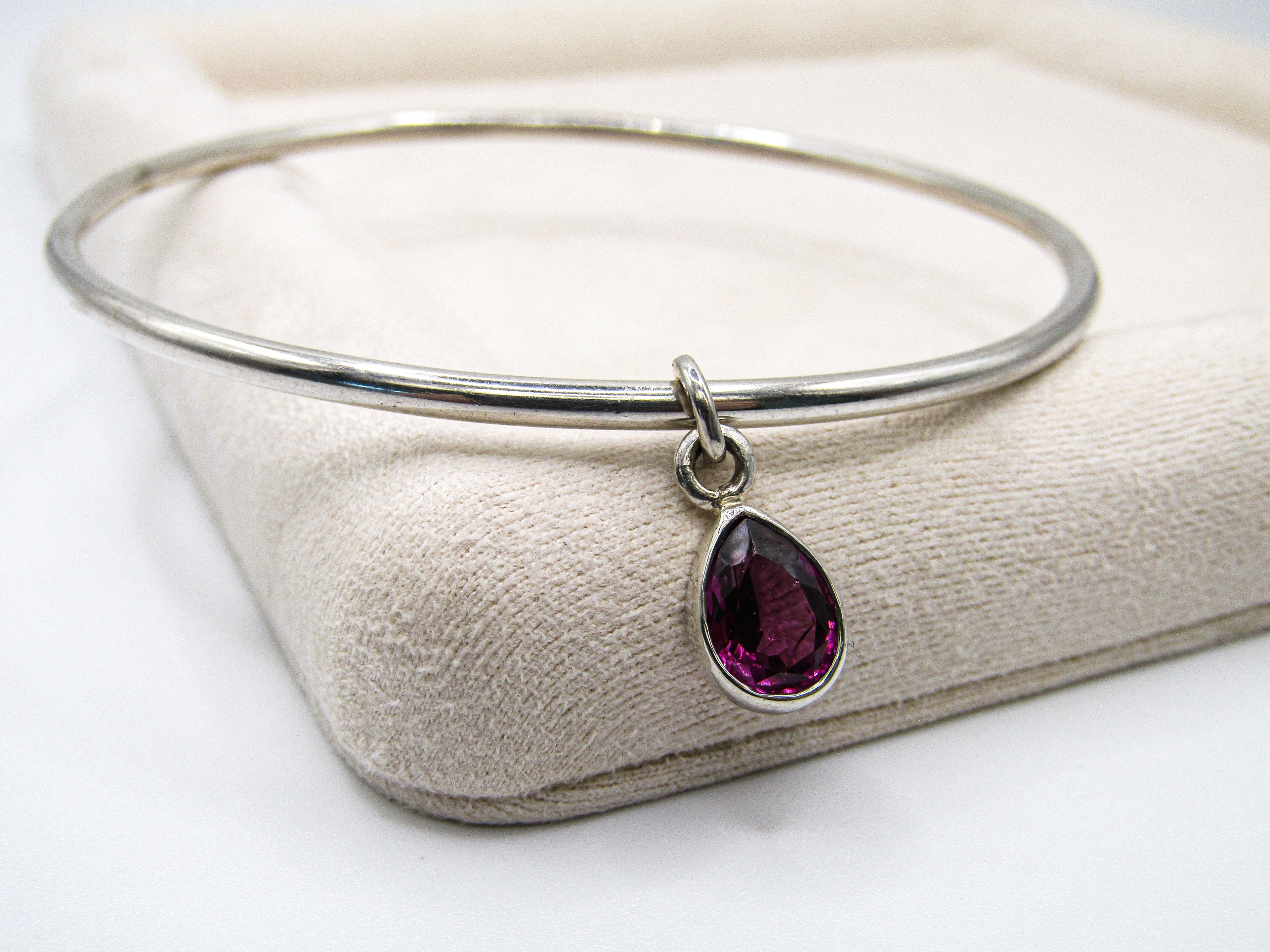 Silver bangle with a teardrop-shaped purple gemstone on a white background
