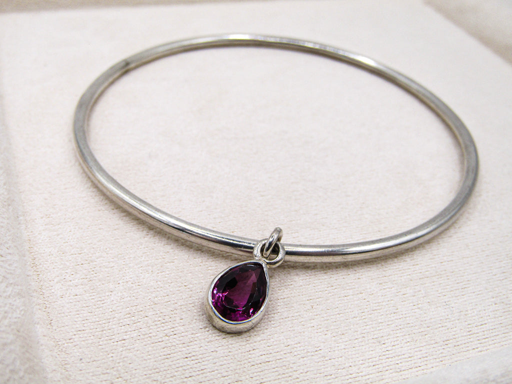 Silver bangle with a purple teardrop pendant on a white fabric background