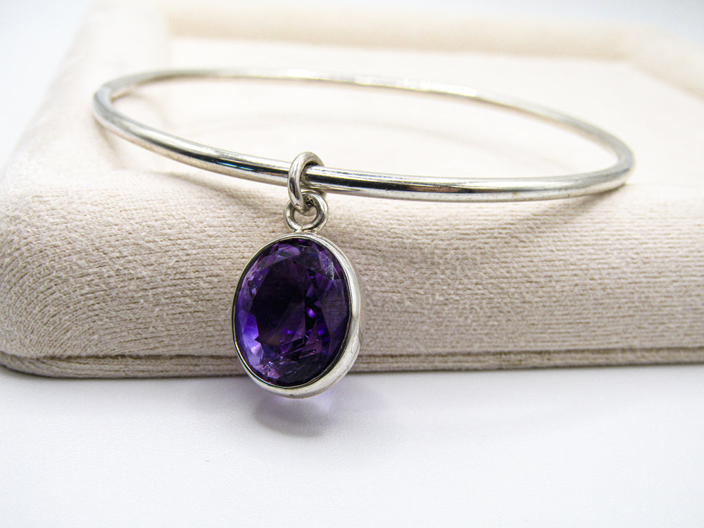 Silver bangle with a purple gemstone on a white background
