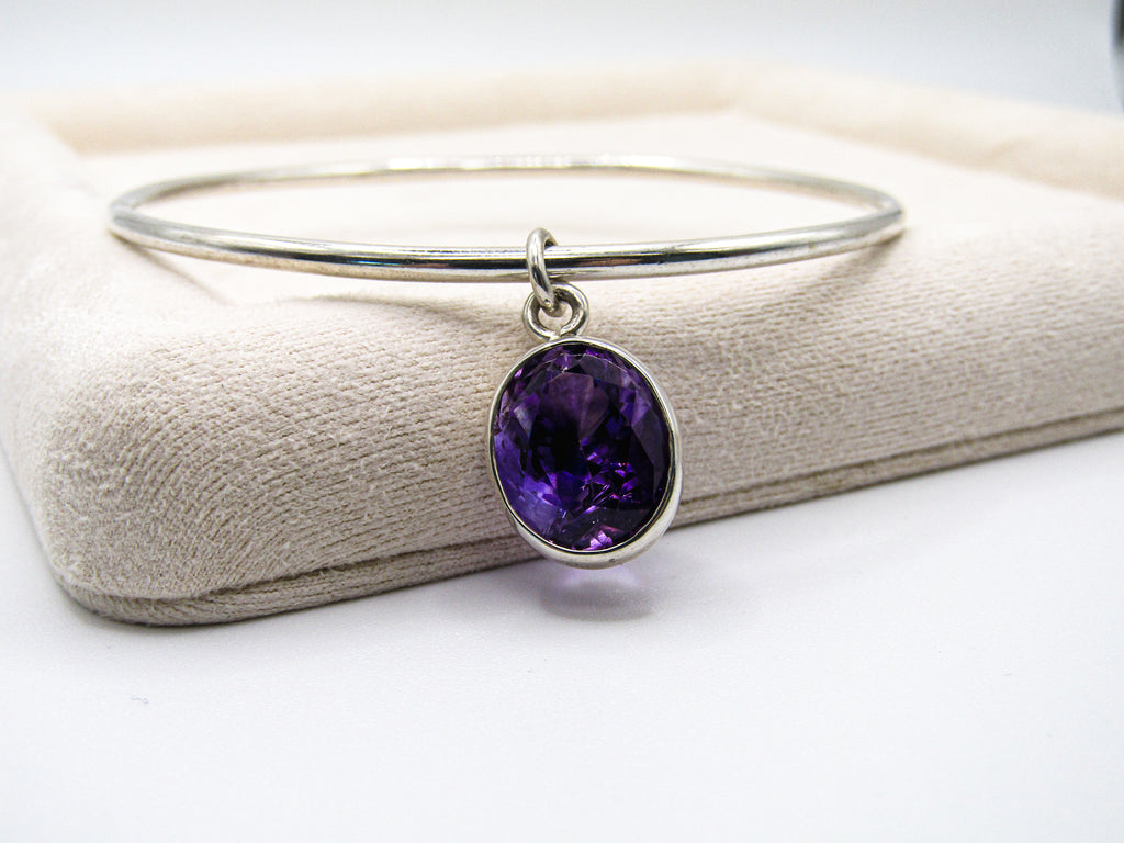 Silver bangle with a purple gemstone on a white background