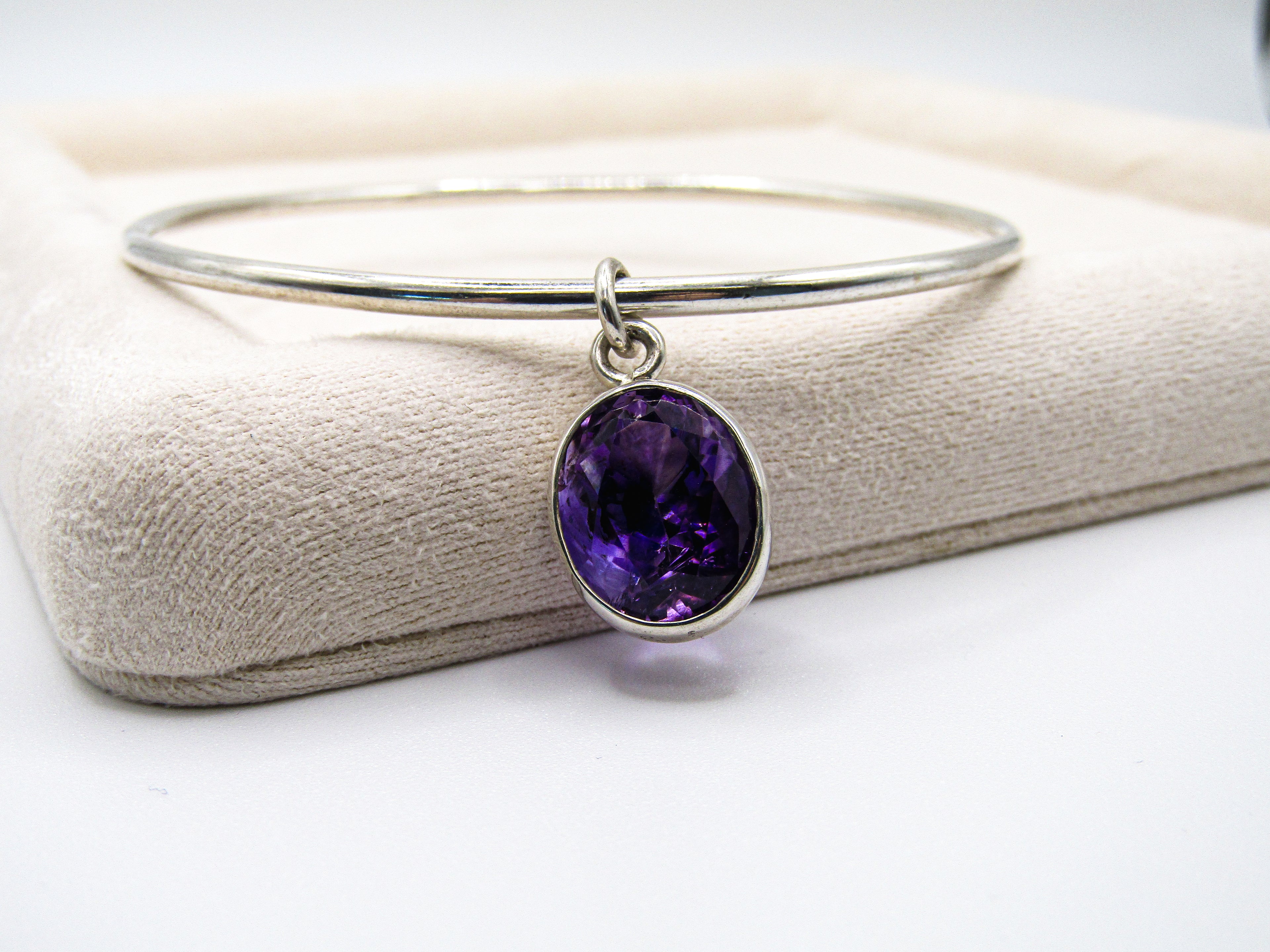Silver bangle with a purple gemstone on a white background