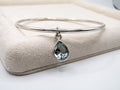 Silver bangle with a teardrop-shaped gemstone on a beige cushion
