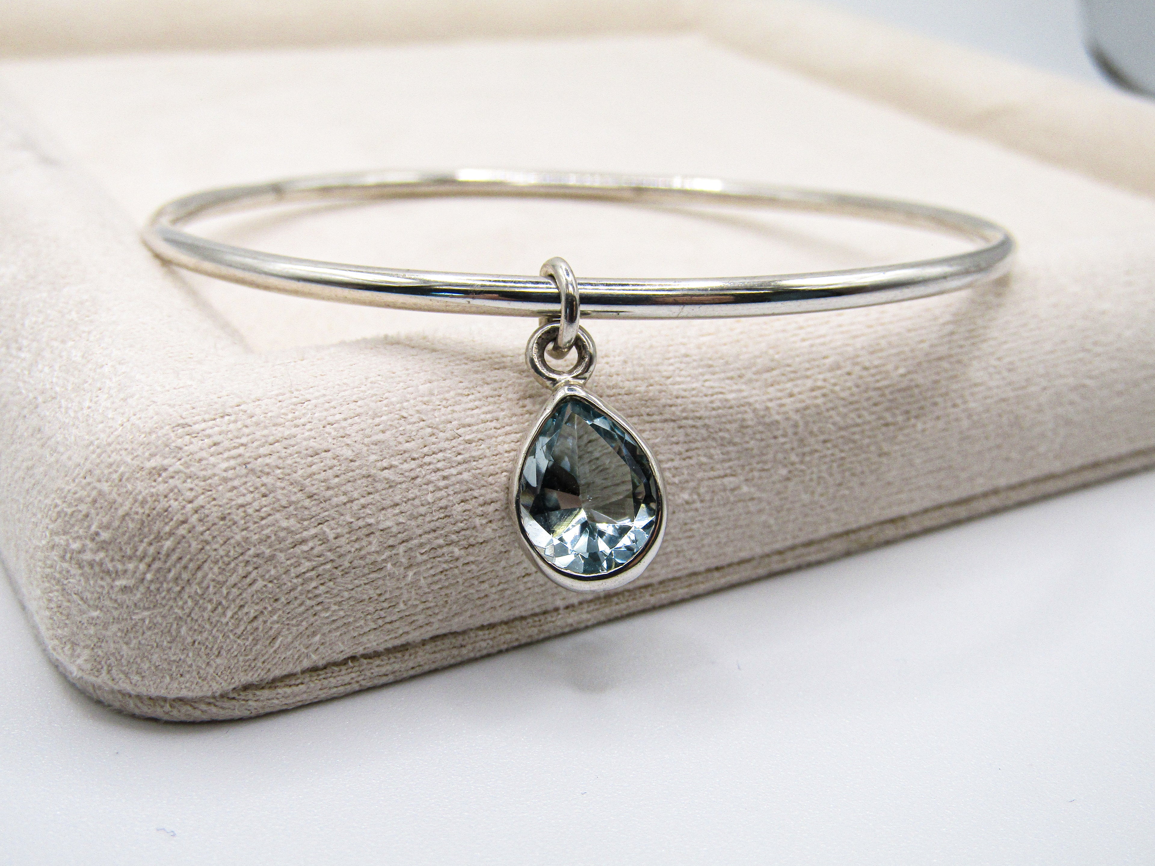 Silver bangle with a teardrop-shaped gemstone on a beige cushion