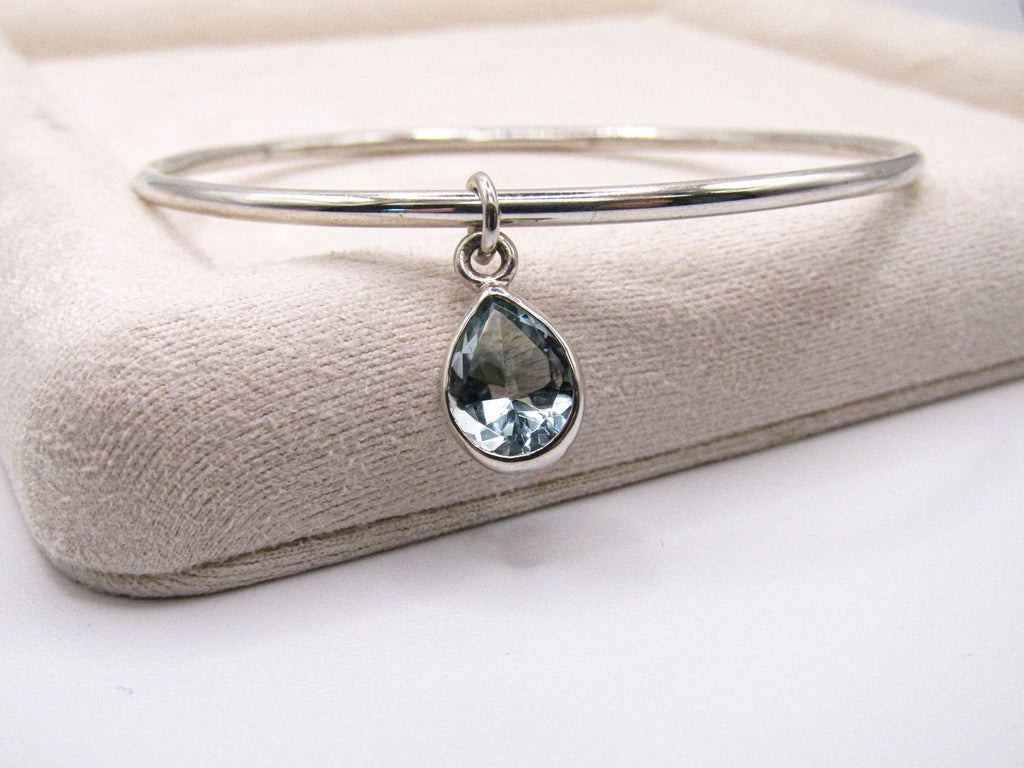 Silver bangle with a teardrop-shaped gemstone on a beige cushion