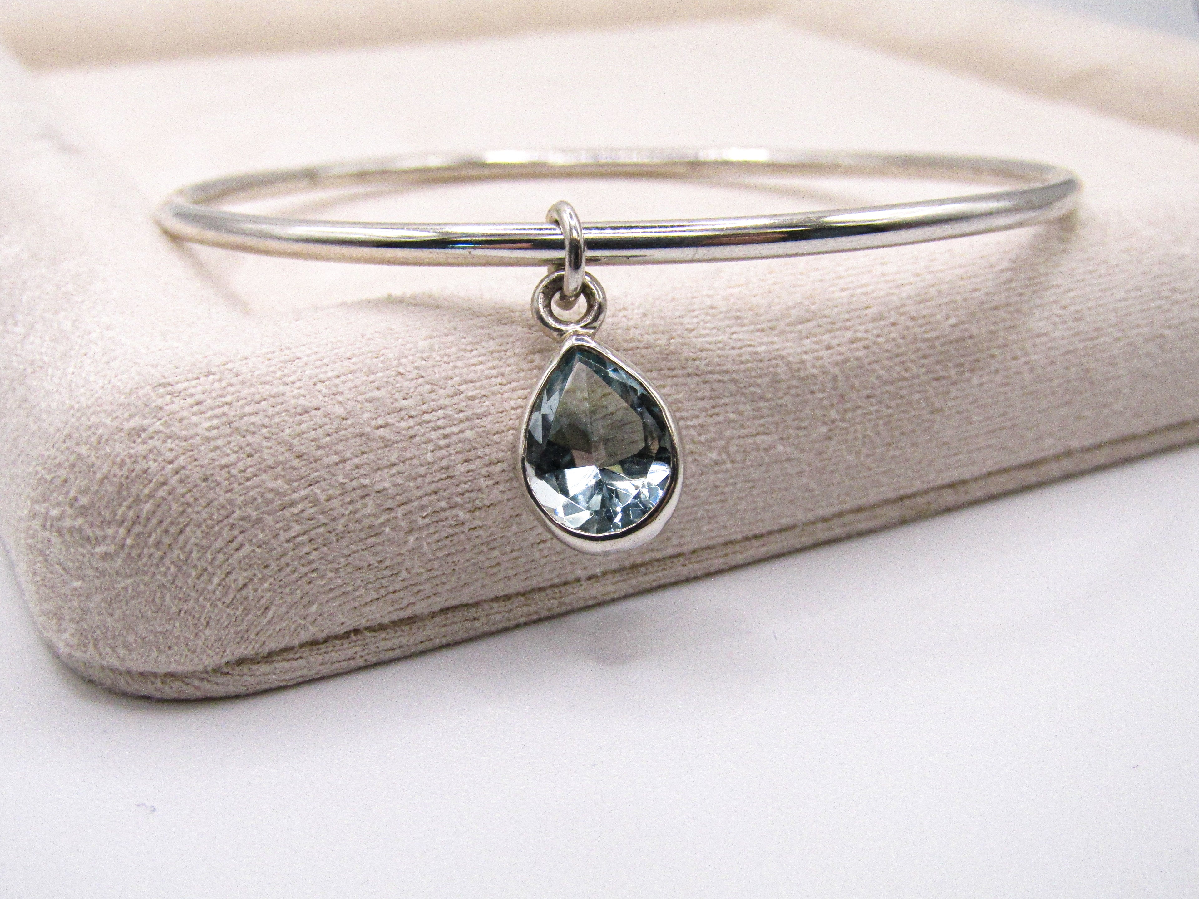 Silver bangle with a teardrop-shaped gemstone on a beige cushion