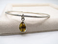 Silver bangle with a teardrop-shaped yellow gemstone on a beige fabric background