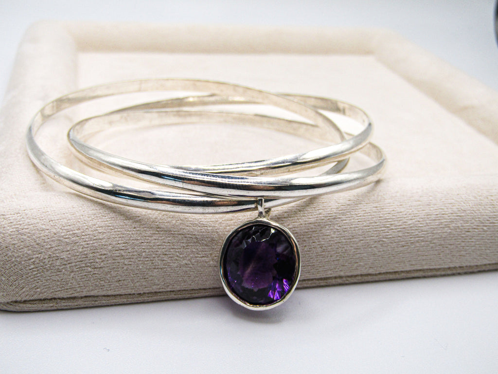 Silver bracelet with a purple gemstone on a beige surface