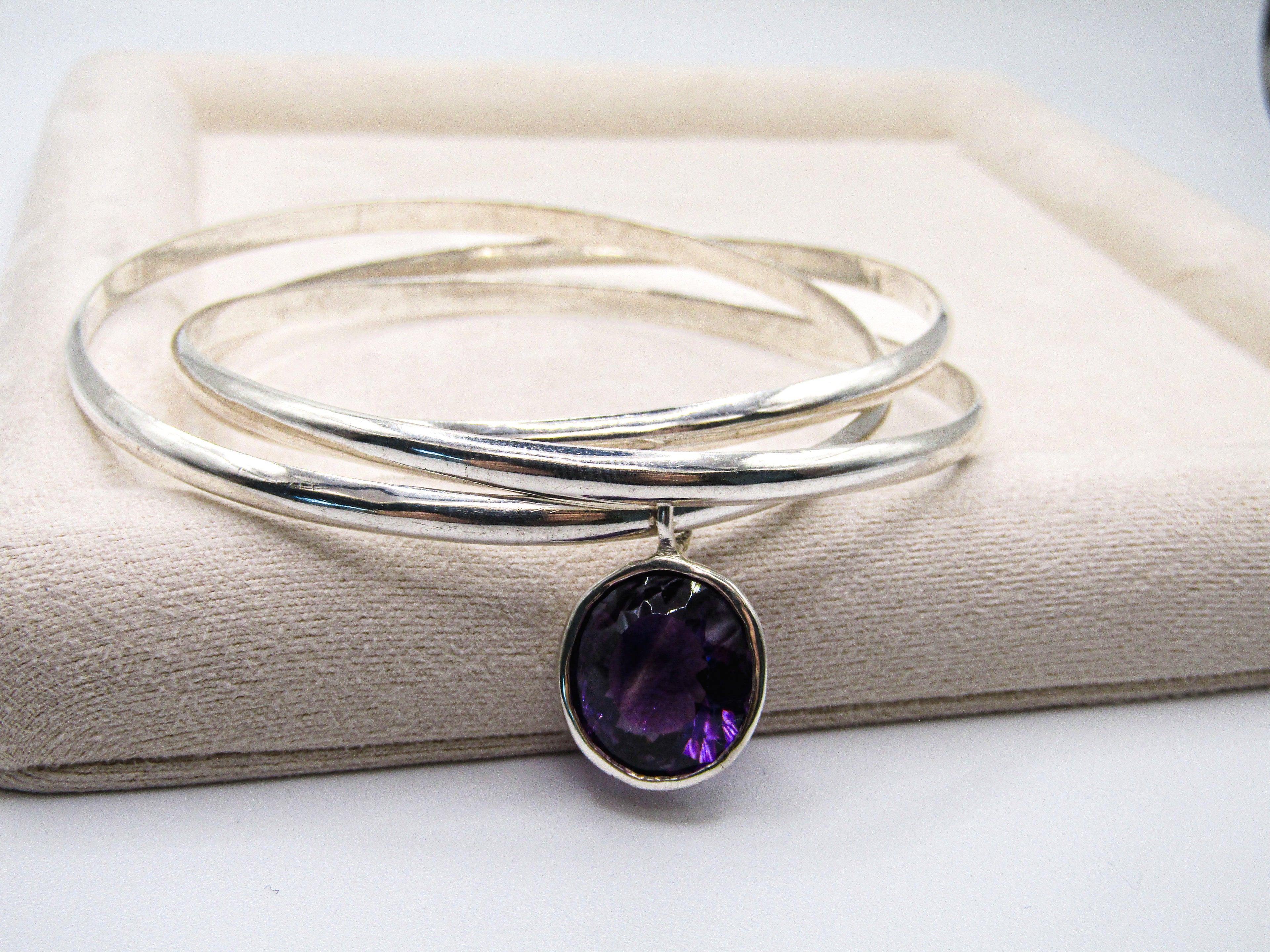 Silver bracelet with a purple gemstone on a beige surface