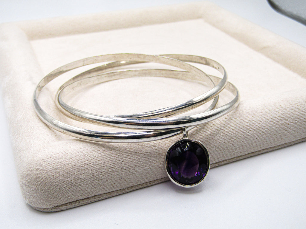 Silver bracelet with a purple gemstone on a beige cushion