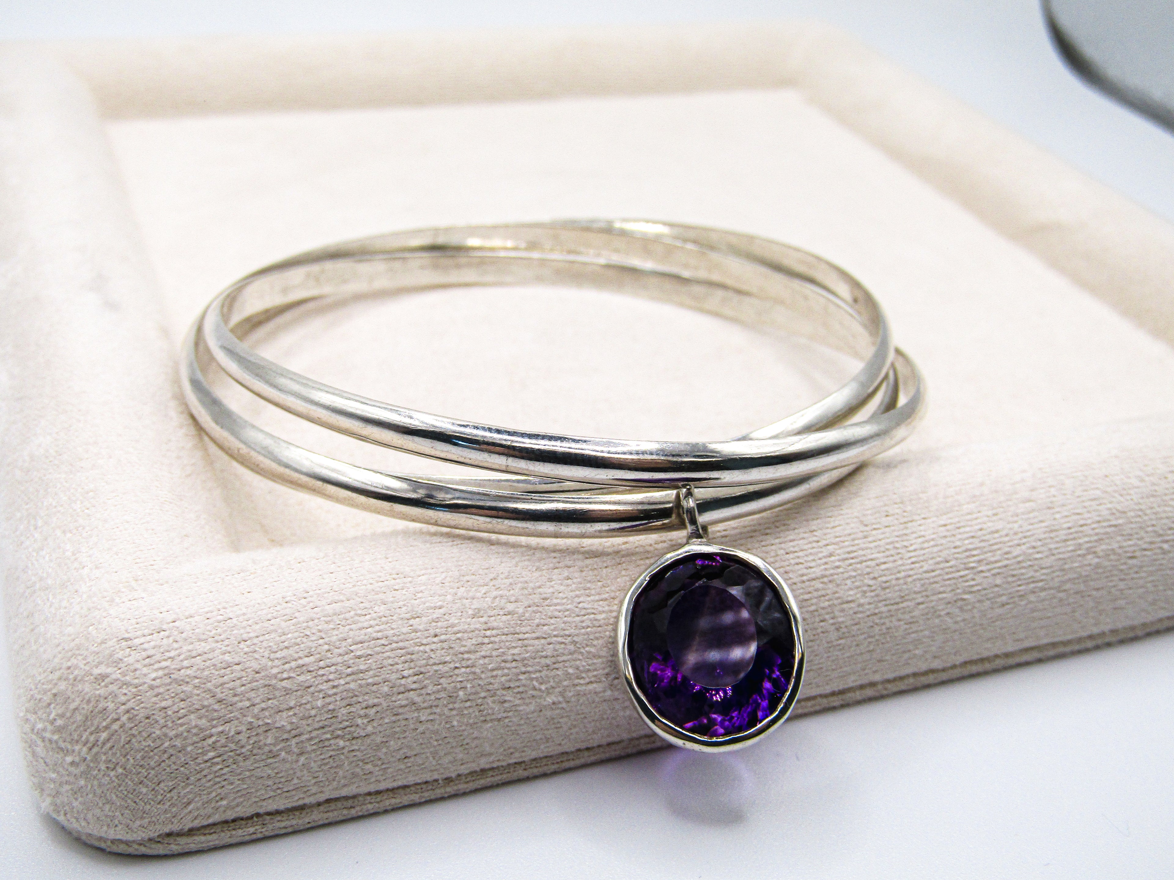 Silver bangle with a purple gemstone on a white cushion