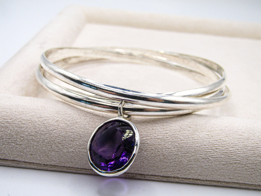 Silver bangle with a purple gemstone on a beige fabric background