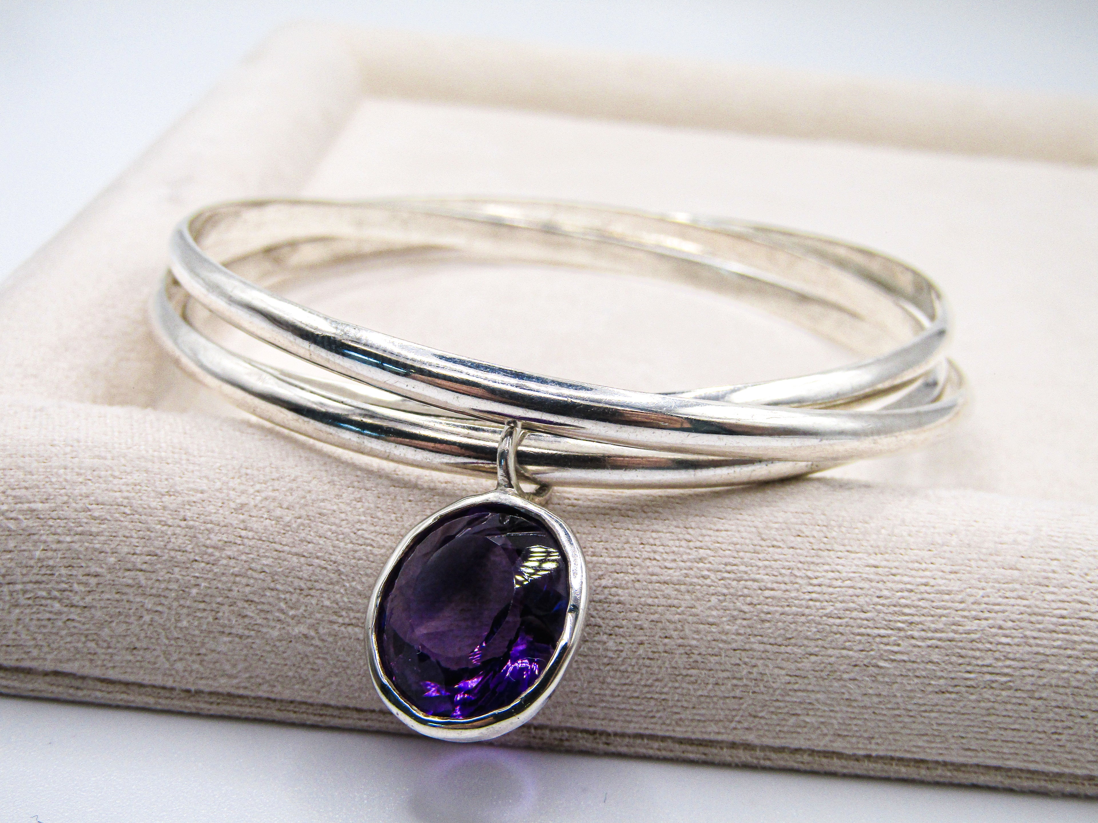 Silver bangle with a purple gemstone on a beige fabric background