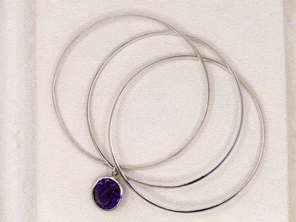 Silver necklaces with a purple pendant on a textured beige background