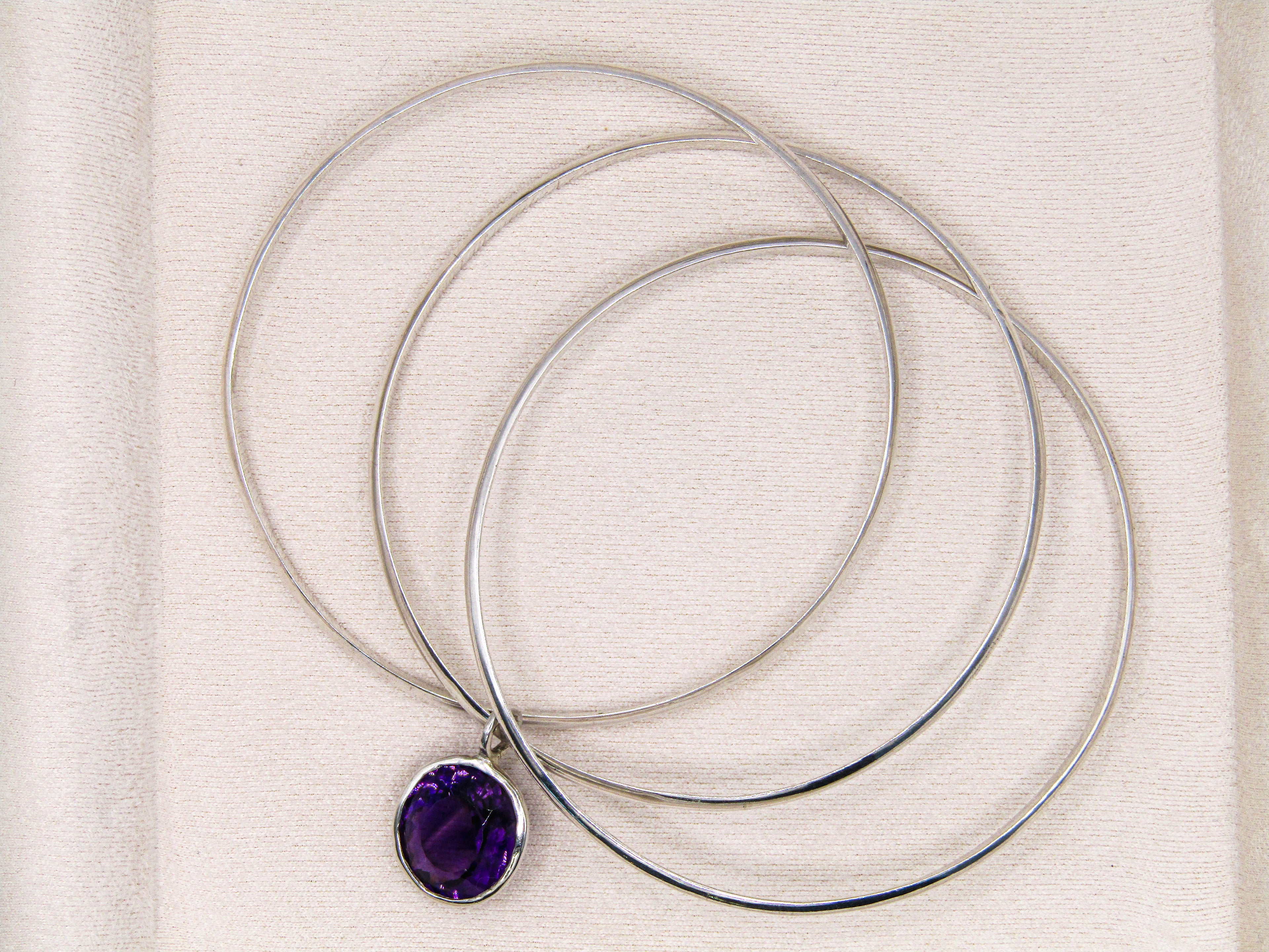 Silver necklaces with a purple pendant on a textured beige background