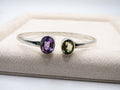 Silver bangle with purple and green gemstones on a textured surface