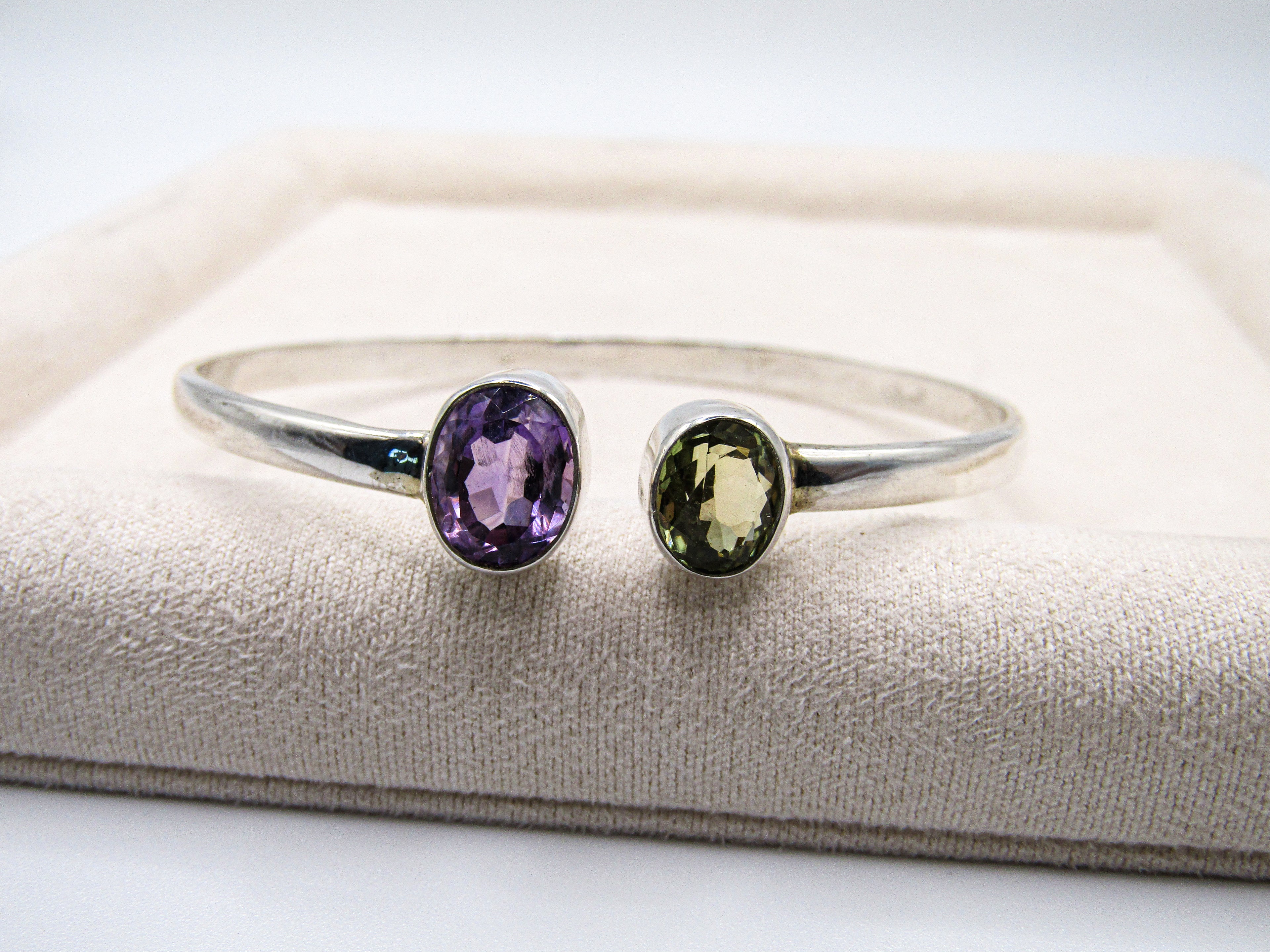 Silver bangle with purple and green gemstones on a textured surface