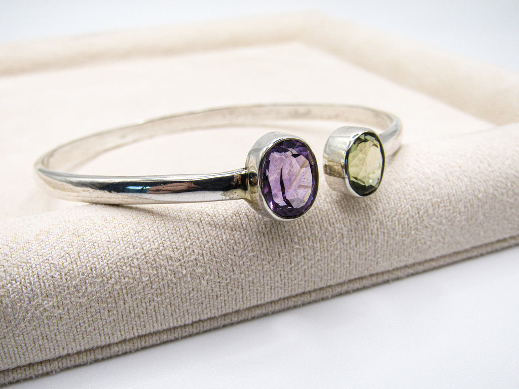 Silver bracelet with purple and green gemstones on a beige cushion