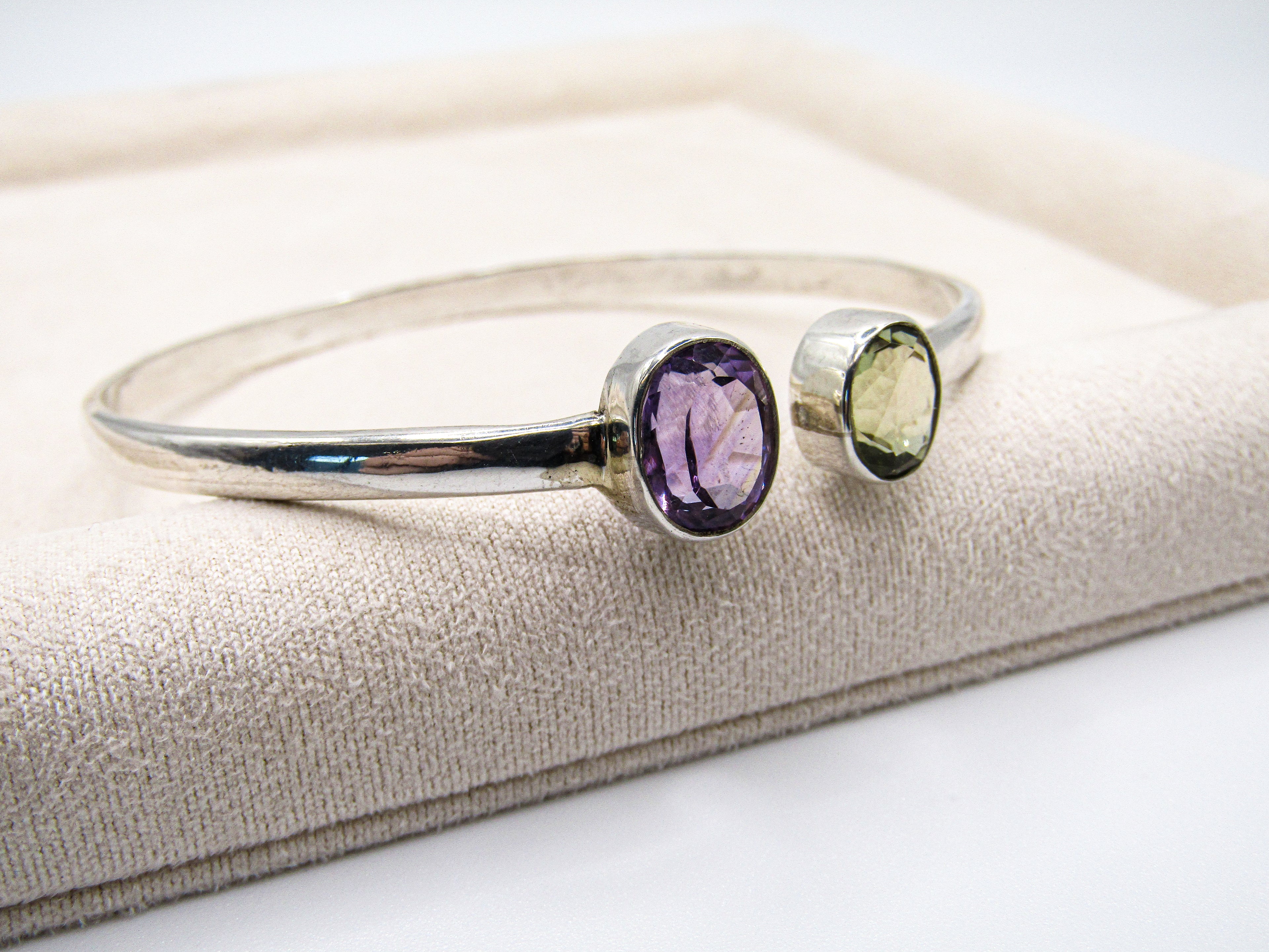 Silver bracelet with purple and green gemstones on a beige cushion