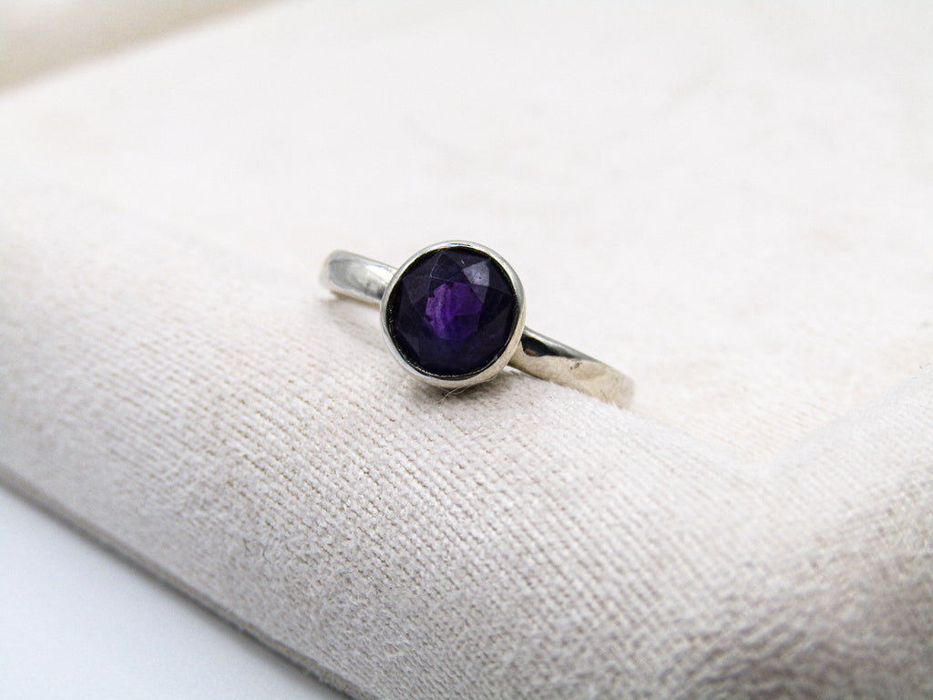 Silver ring with a purple gemstone on a white surface