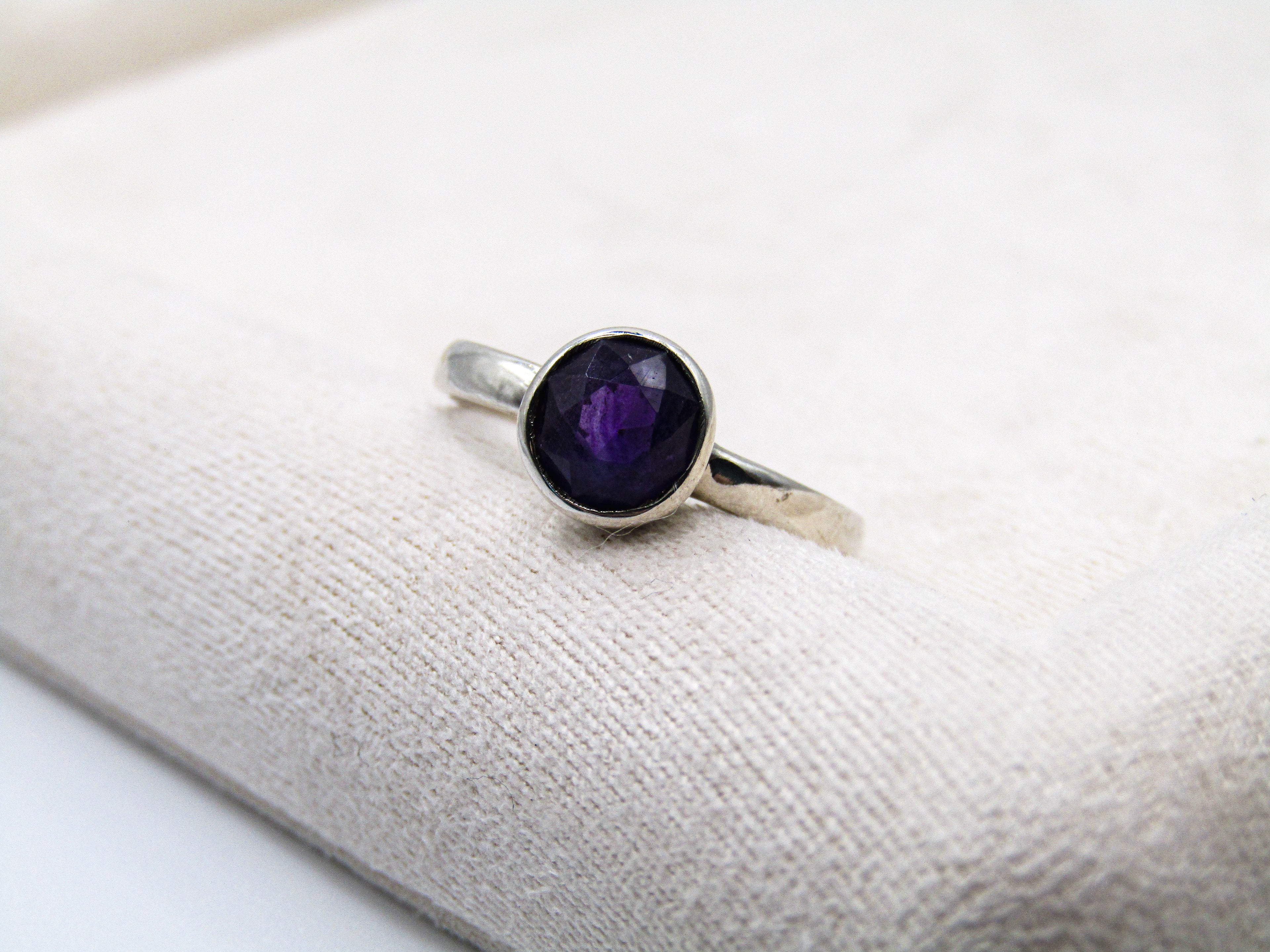 Silver ring with a purple gemstone on a white surface