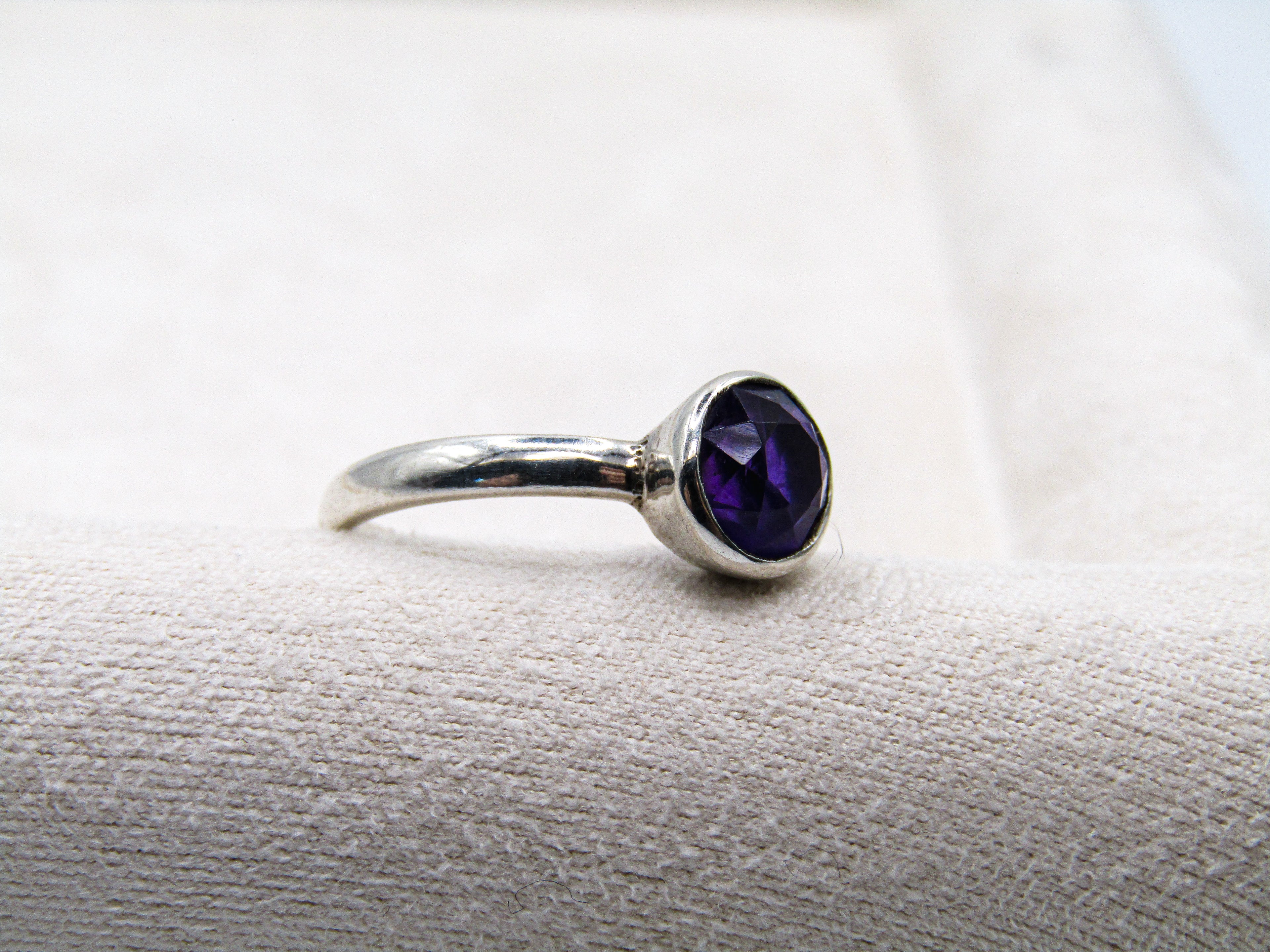 Silver ring with a purple gemstone on a textured surface