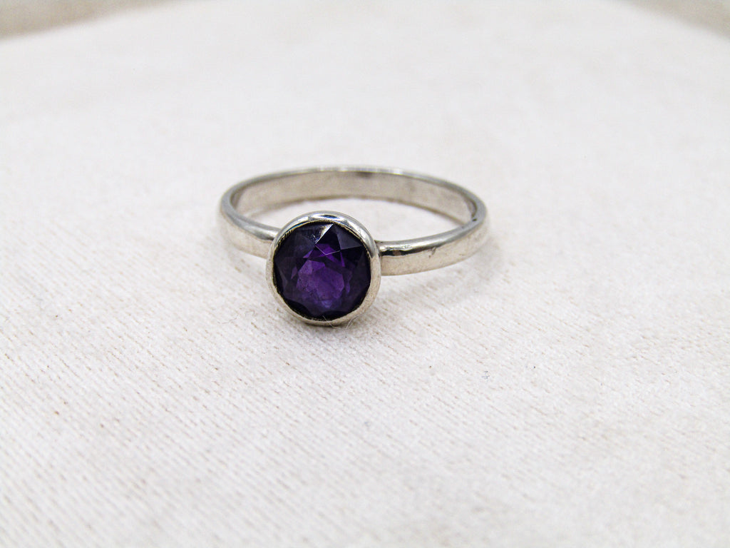 Silver ring with a purple gemstone on a white fabric background
