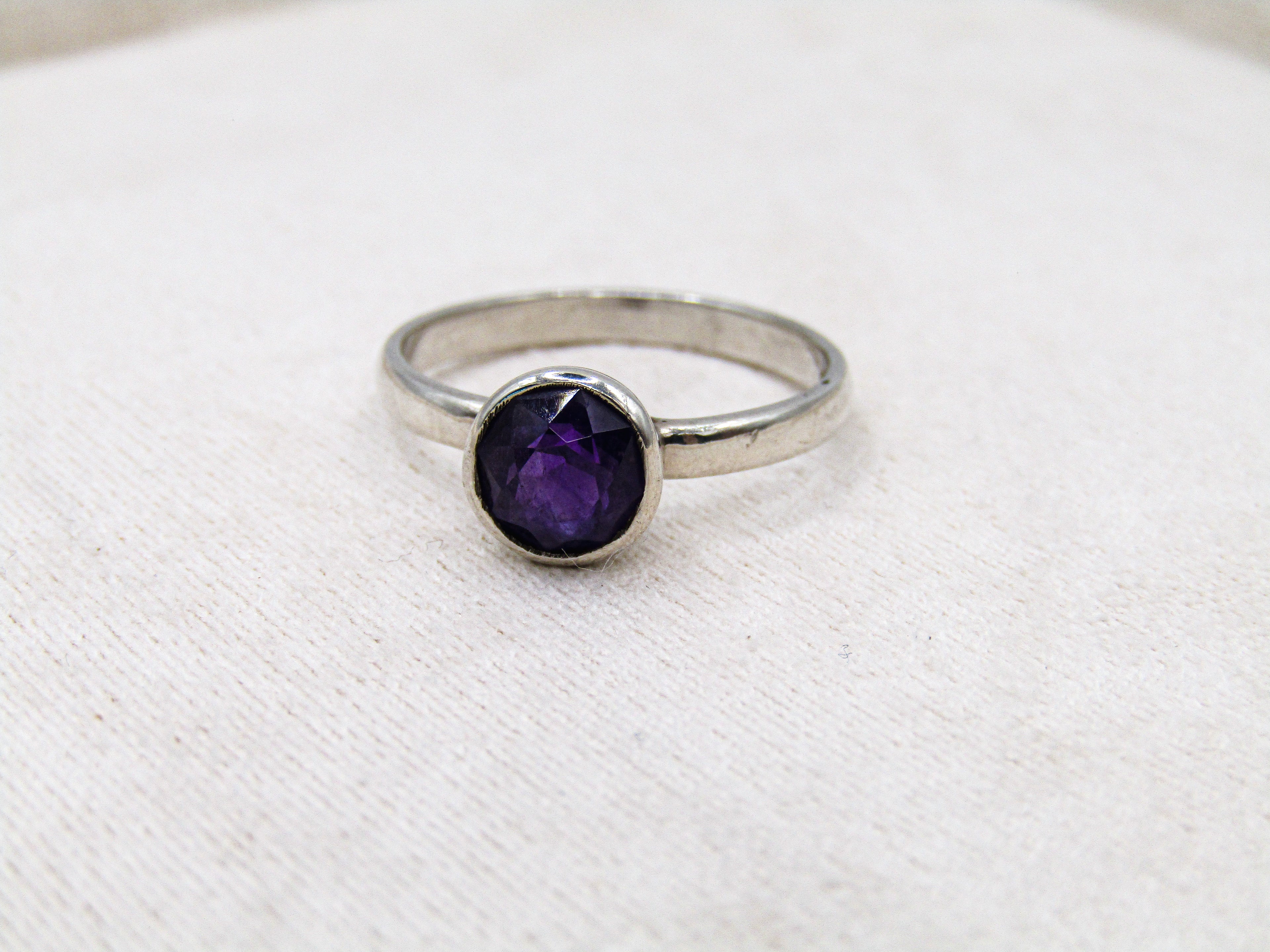 Silver ring with a purple gemstone on a white fabric background