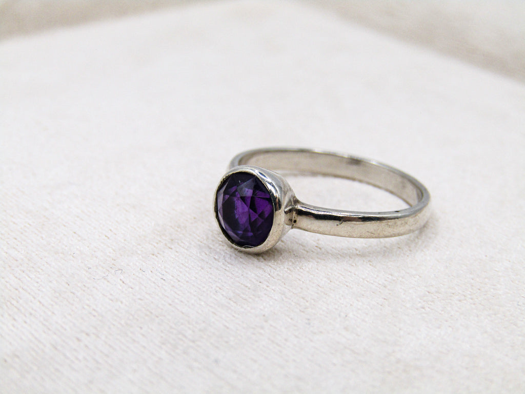 Silver ring with a purple gemstone on a white fabric background