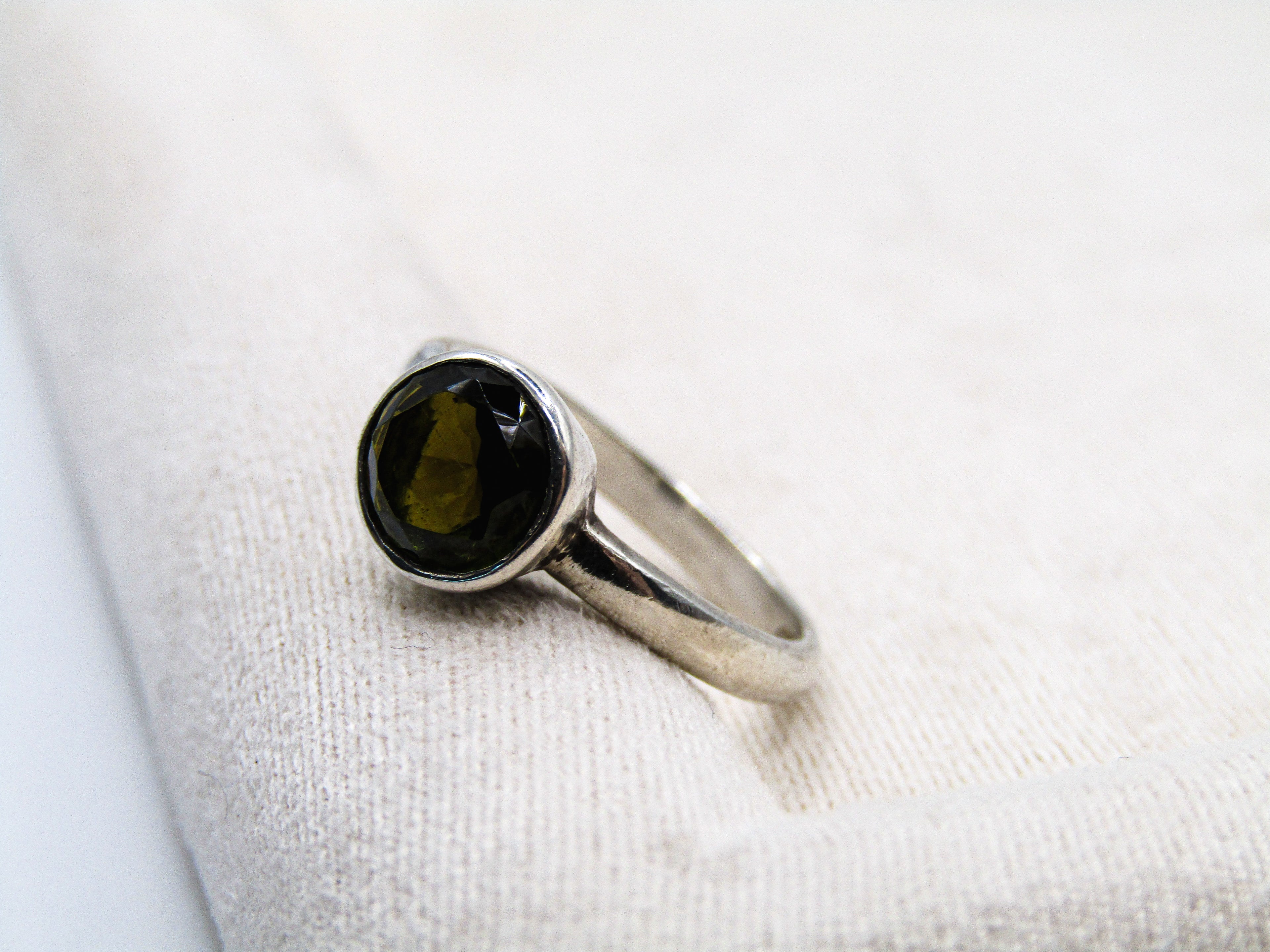 Silver ring with a dark gemstone on a white fabric background