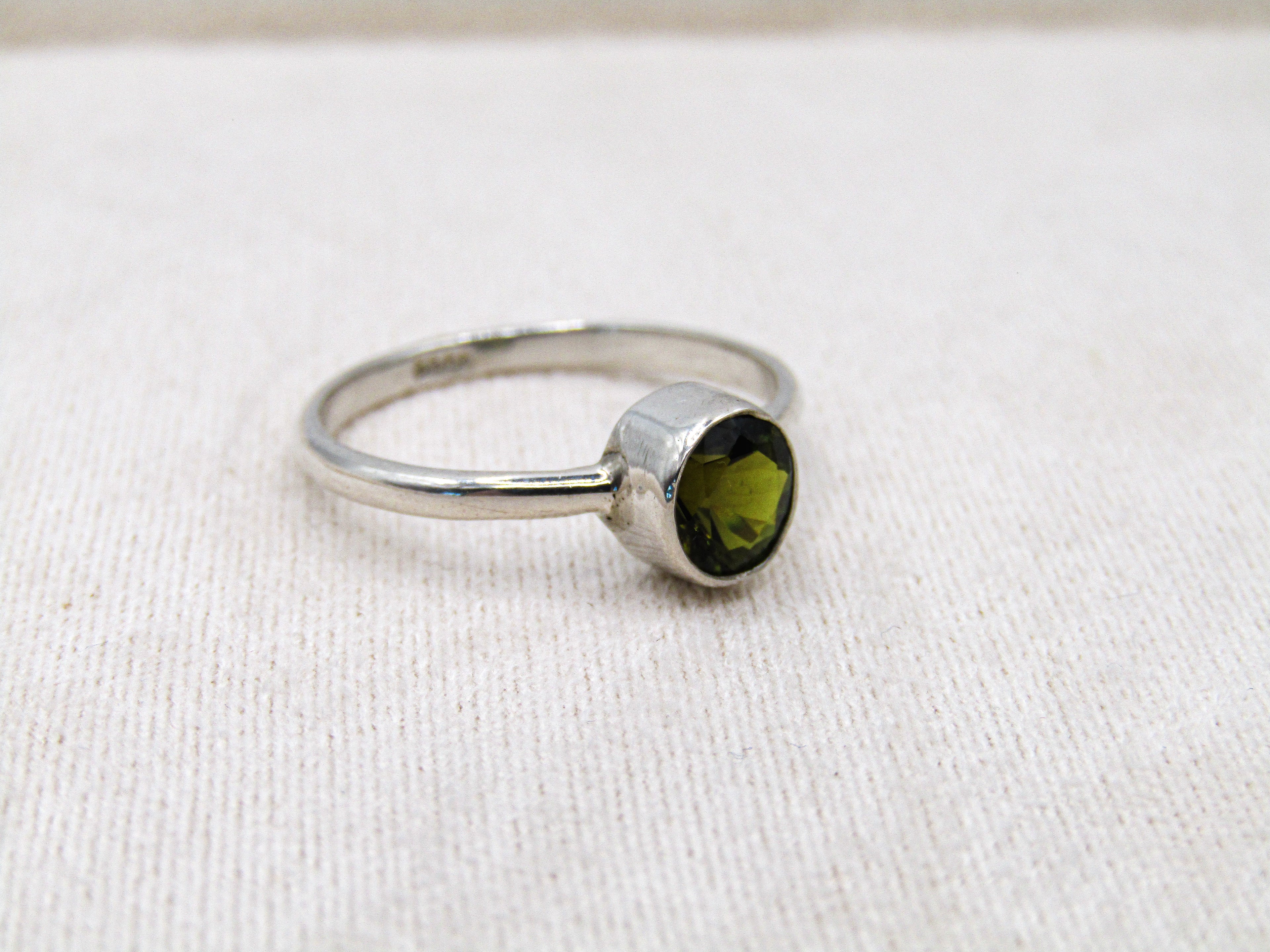 Silver ring with a green gemstone on a white fabric background