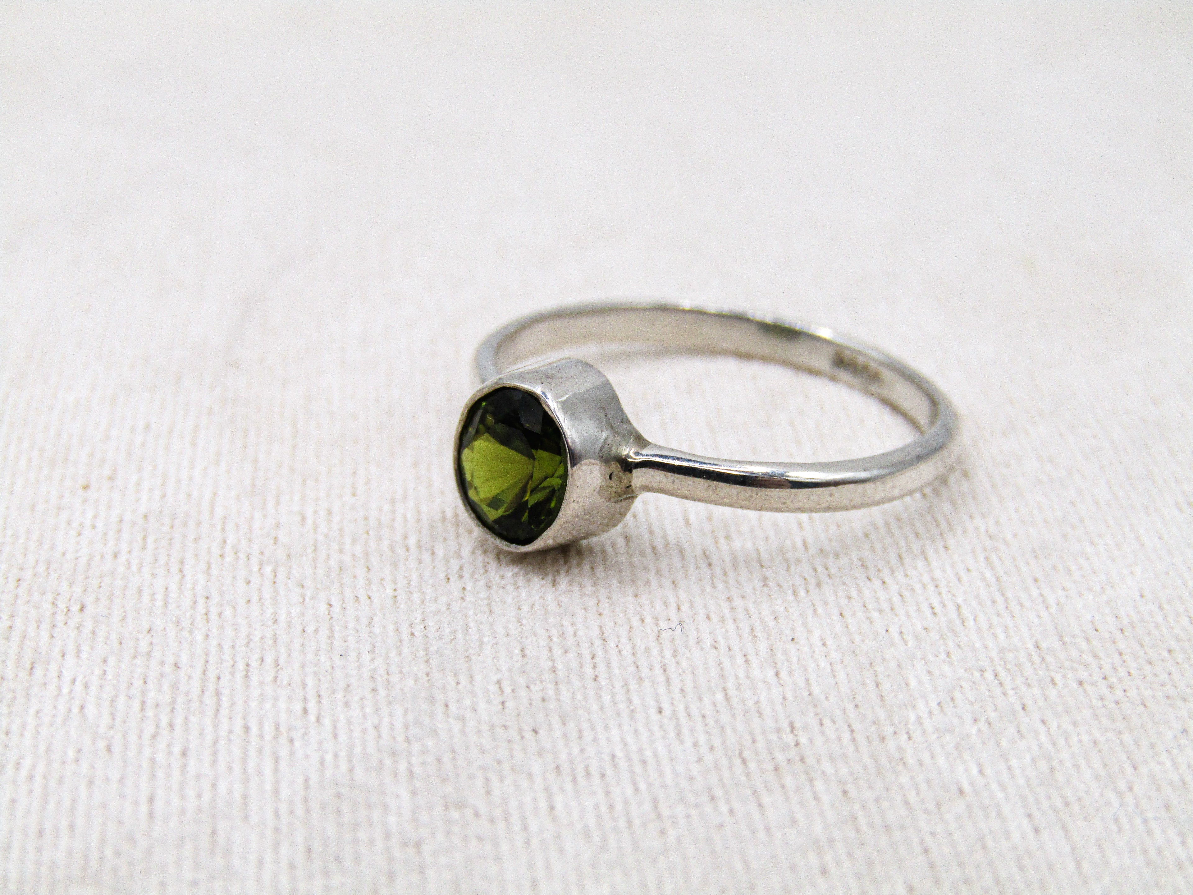 Silver ring with a green gemstone on a white fabric background