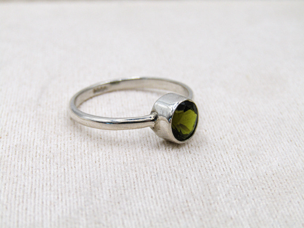 Silver ring with a green gemstone on a white fabric background