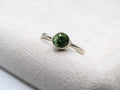 Silver ring with a green gemstone on a white fabric background