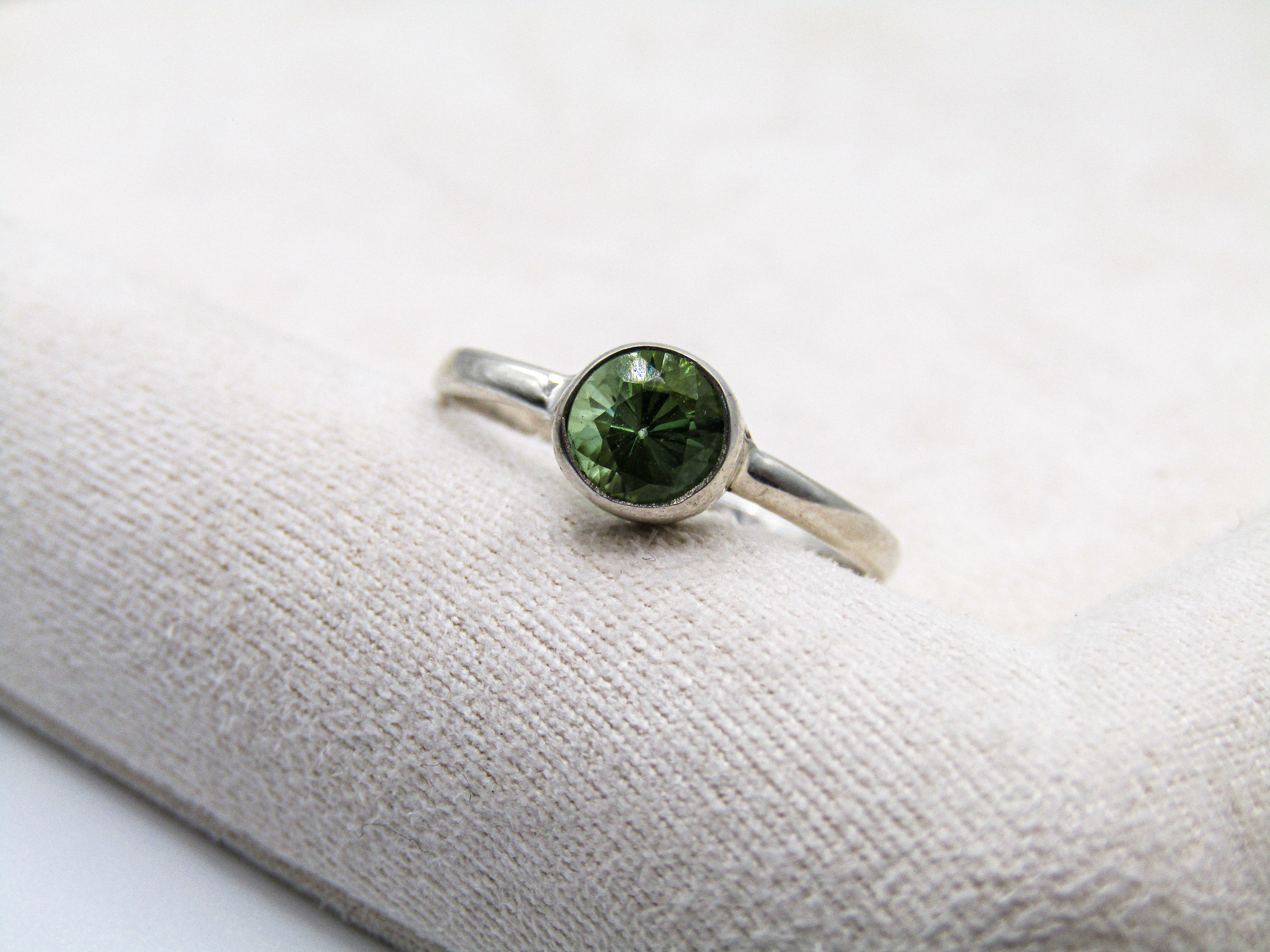 Silver ring with a green gemstone on a white fabric background
