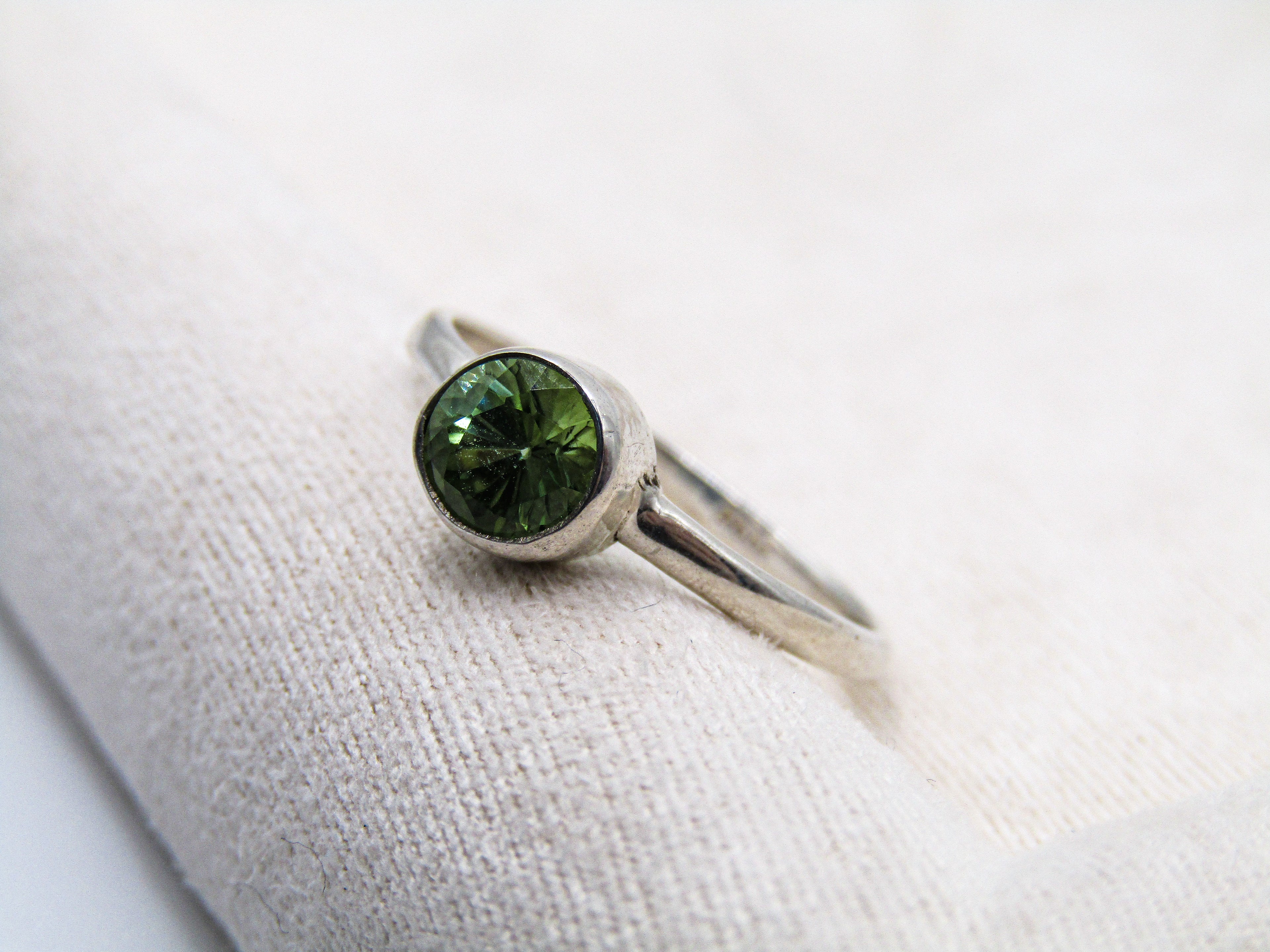 Silver ring with a green gemstone on a white fabric background