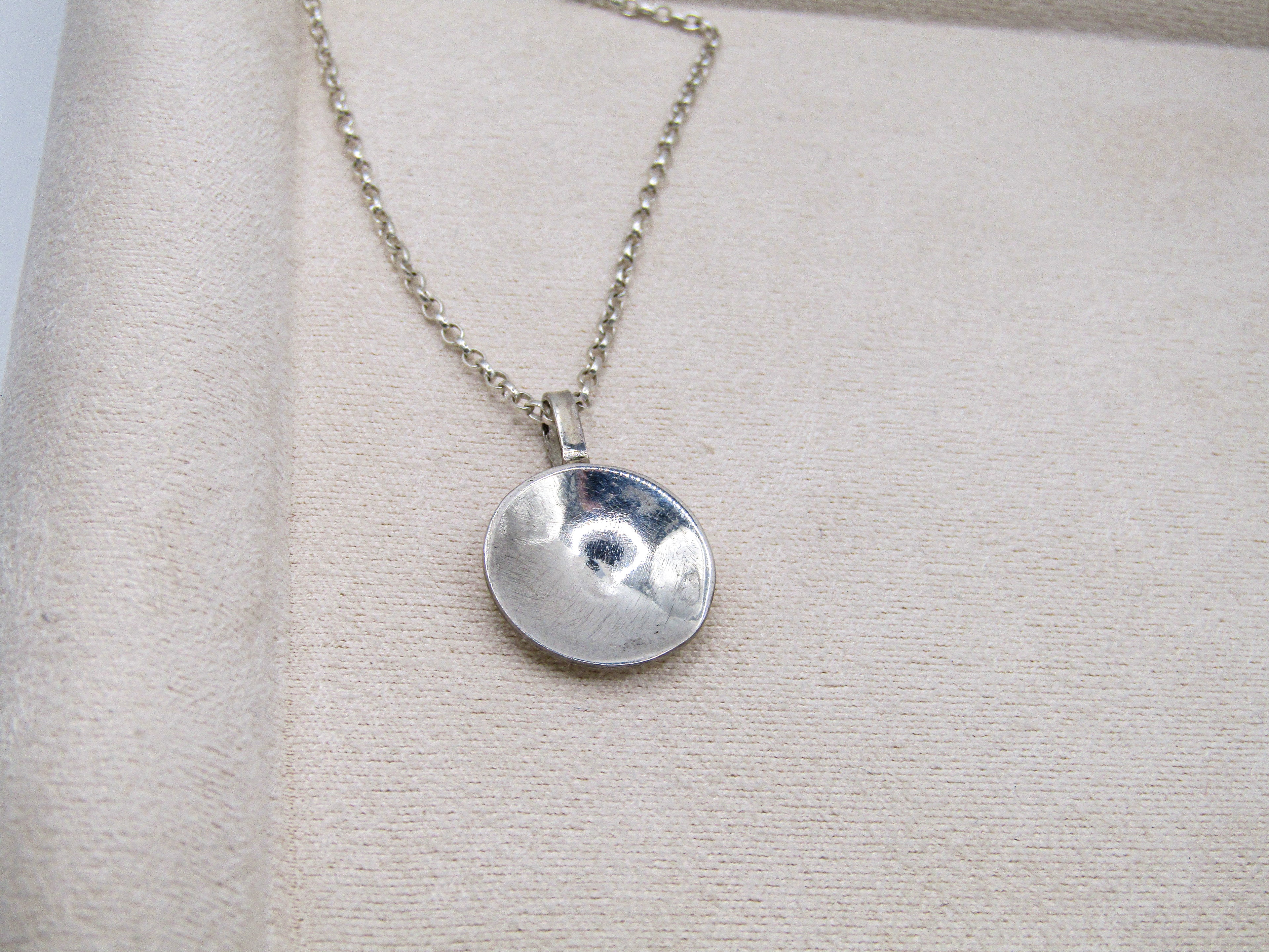 Silver necklace with a round pendant on a light gray background