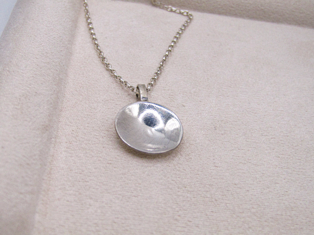 Silver necklace with a round pendant on a beige fabric background