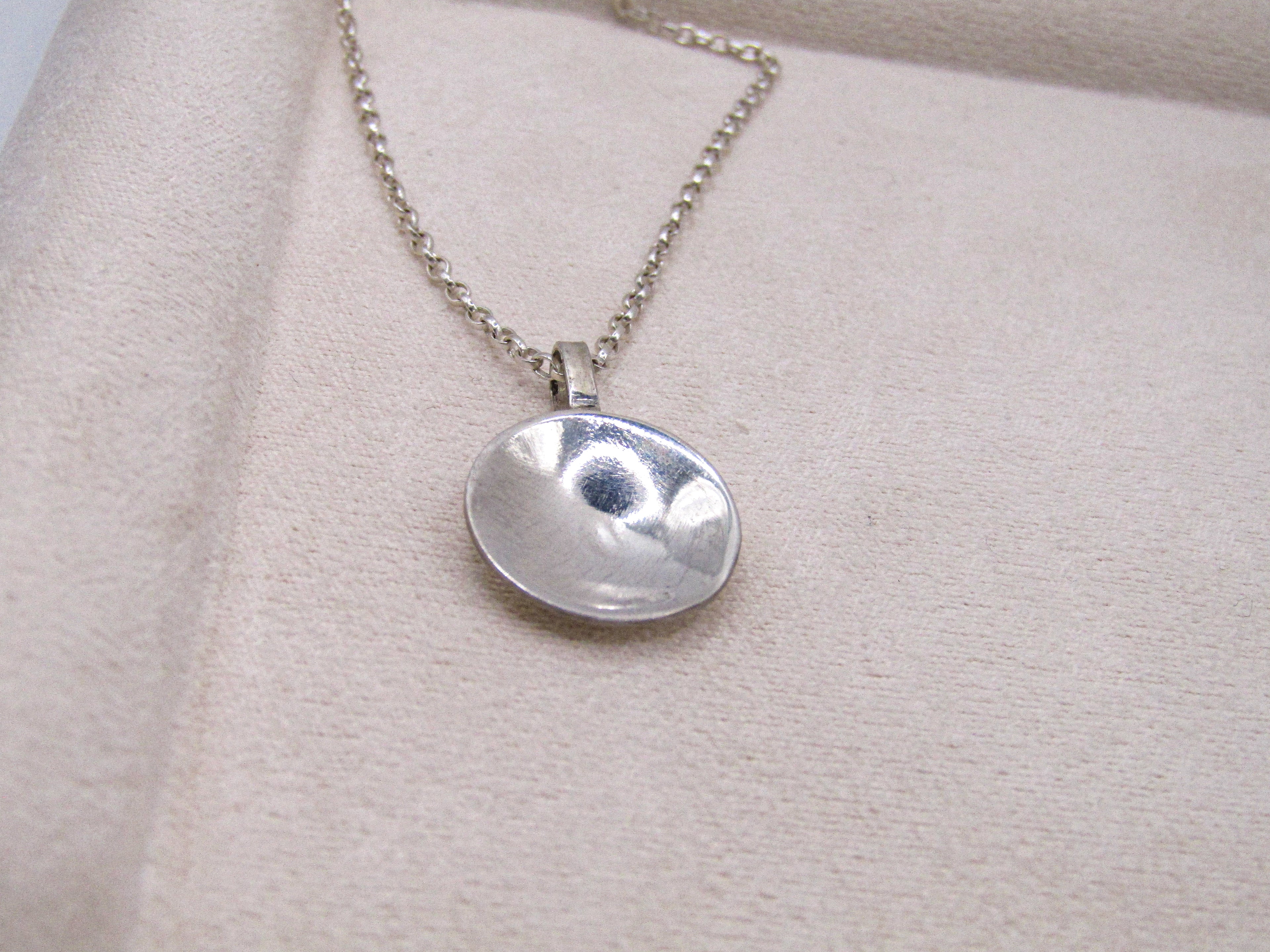 Silver necklace with a round pendant on a beige fabric background