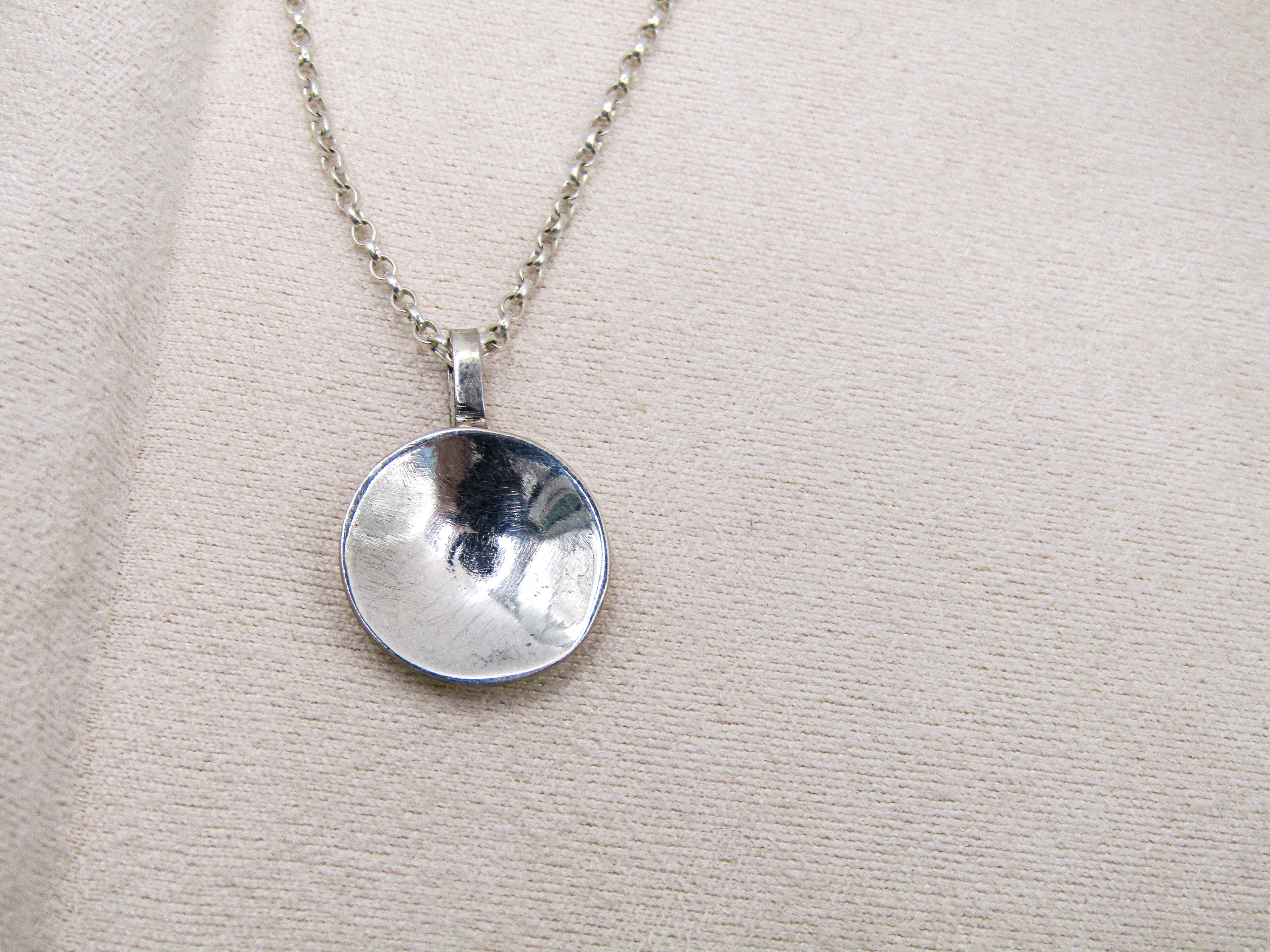 Silver pendant necklace on a beige fabric background