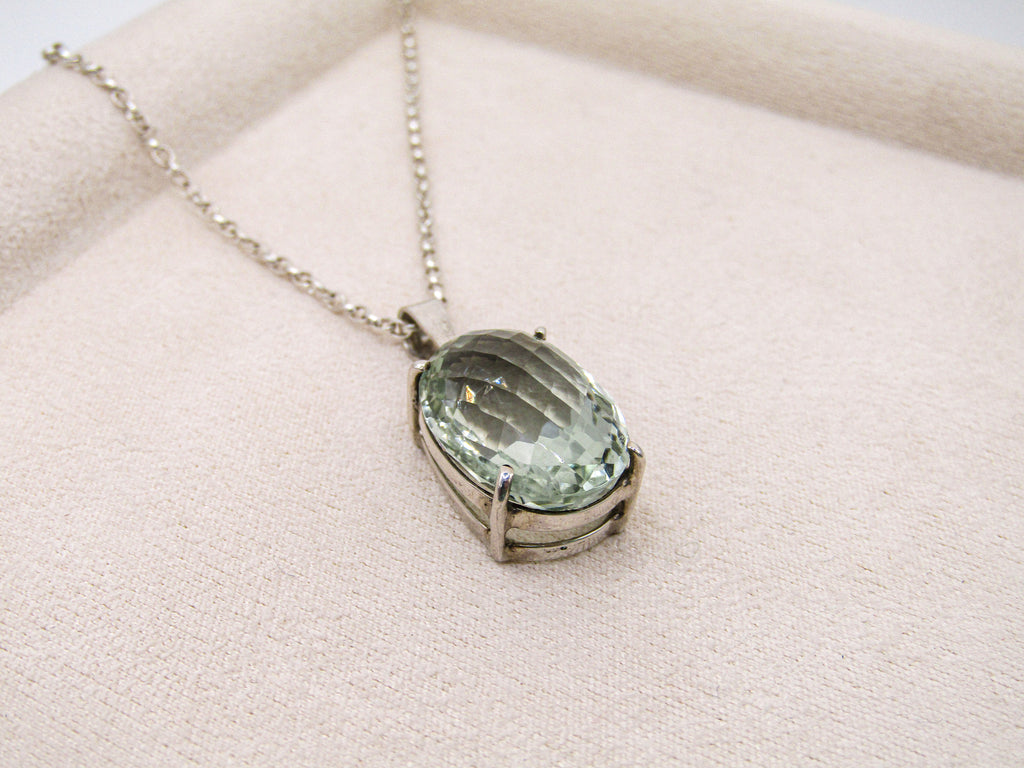Necklace with a green gemstone pendant on a light pink surface