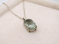 Necklace with a green gemstone pendant on a light pink surface