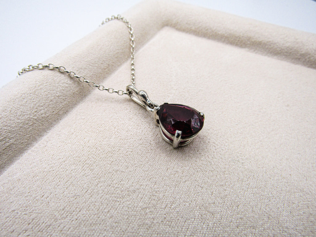 Necklace with a teardrop-shaped purple gemstone on a beige fabric background