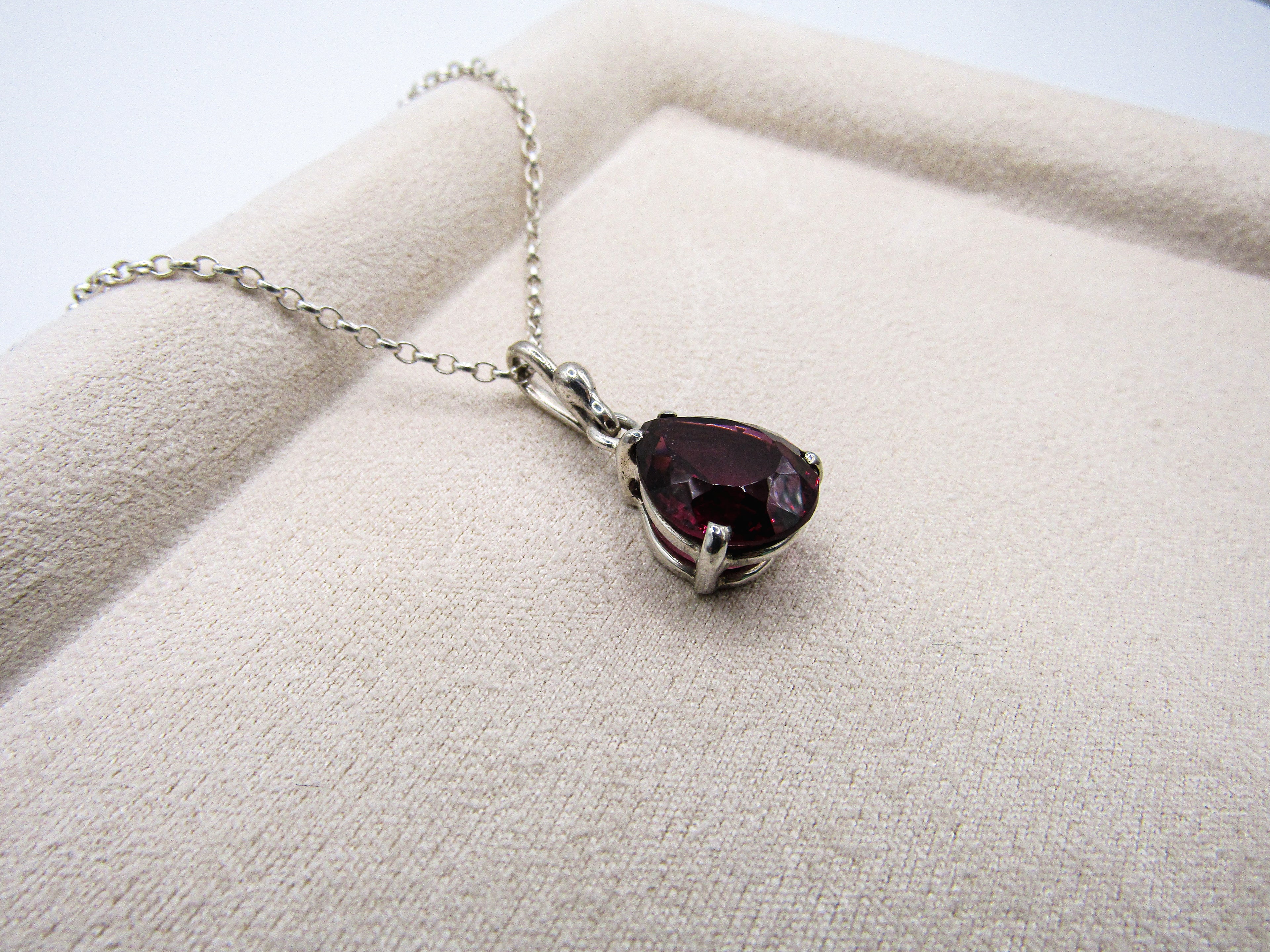 Necklace with a teardrop-shaped purple gemstone on a beige fabric background